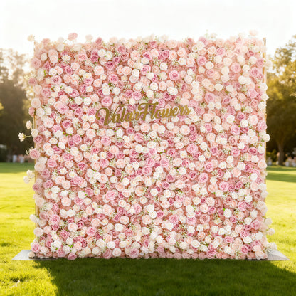 This image showcases a stunning floral backdrop by Valar Flowers, set outdoors on a lush lawn. It features a dense arrangement of artificial roses in soft pink and peach tones, with the brand’s name elegantly displayed in gold. Bathed in sunlight, with a scenic park in the background, it exudes elegance, perfect for adding a luxurious, nature-inspired element to outdoor events.