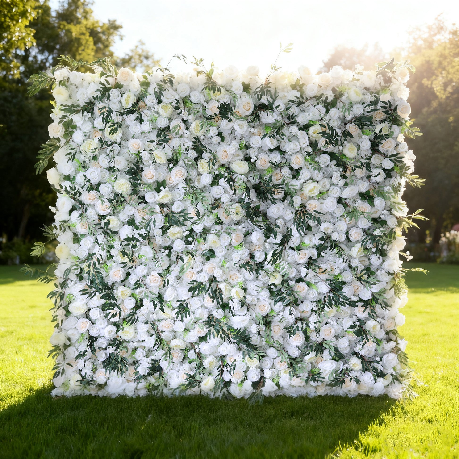 This image showcases a stunning floral wall by Valar Flowers, set outdoors on a lush green lawn. It features a dense arrangement of artificial flowers in soft shades of white and cream, interspersed with lush green foliage. The meticulously crafted blooms create a lush, elegant, and visually soothing display. Bathed in sunlight, this floral wall is perfect for adding a touch of timeless beauty to events or spaces, exuding a refined and sophisticated atmosphere.