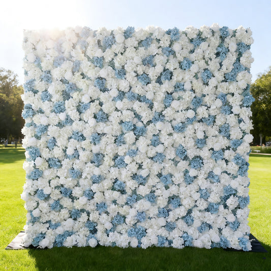 This image features a large, square floral wall composed of white and light blue flowers. Set outdoors on a lush green lawn under a bright sky, the dense arrangement of blooms creates a soft, elegant, and refreshing look. It's perfect for decorative purposes, such as events or photo backdrops, exuding a serene and charming atmosphere.