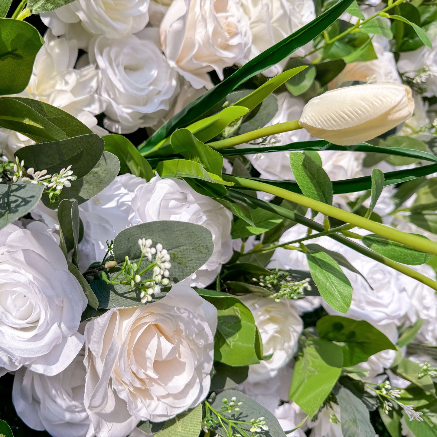 This photo showcases a lush arrangement of white roses and tulips, interspersed with green foliage. The delicate white blooms create an elegant and serene display. Ideal for events like a “White Elegance” wedding or a refined garden party, it exudes a sense of purity and sophistication, perfect for upscale and graceful celebrations. 