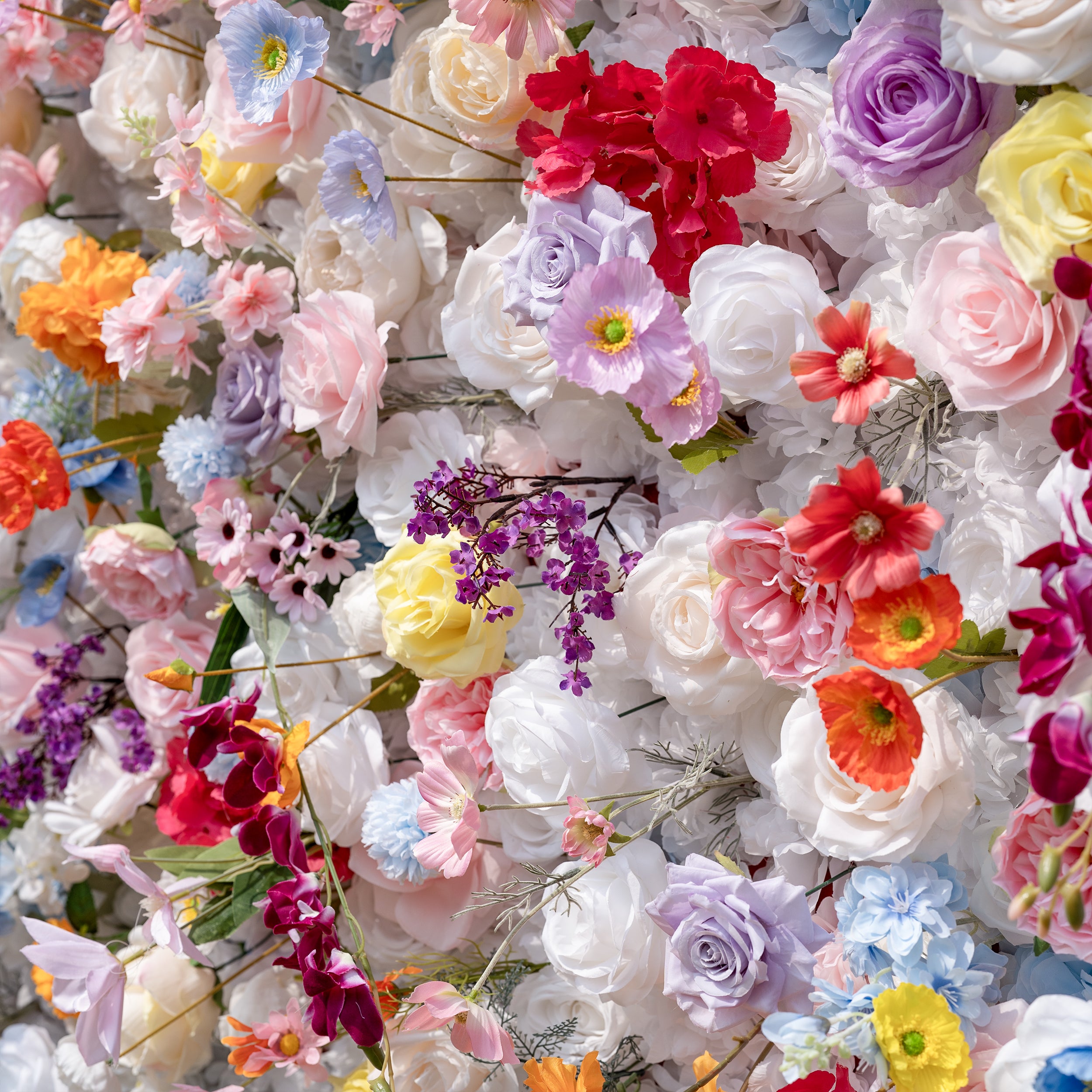 This is a lush, vibrant close-up of a premium artificial mixed-flower wall, brimming with lifelike blooms in a joyful rainbow palette. It features creamy white roses, soft pink peonies, sunny yellow roses, vivid orange carnations, sky-blue poppies, lavender roses, deep red hydrangeas, and delicate purple filler flowers. The layered, realistic petals create a dreamy, romantic, whimsical aesthetic, perfect for wedding backdrops, event decor, and photo booth styling.