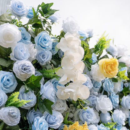 This is a lush, premium artificial flower wall arrangement, brimming with lifelike blooms in a dreamy cool-toned palette. It features sky-blue roses, creamy white roses, elegant white phalaenopsis orchids, sunny yellow roses, and vibrant green foliage. The dense, realistic design creates a fresh, elegant, romantic focal point, perfect for wedding backdrops, photo booths, bridal showers, and luxury event decor.