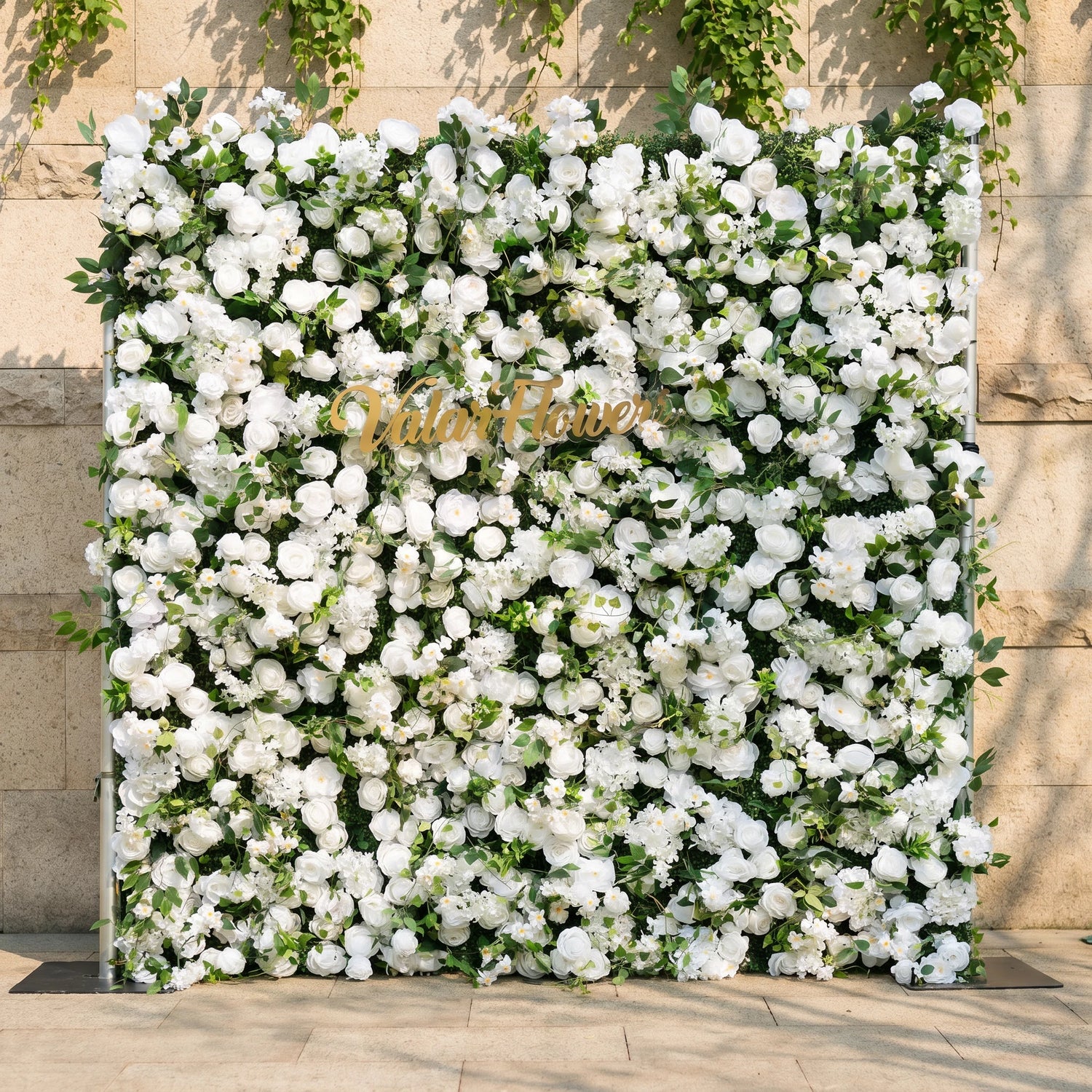 This stunning artificial flower wall backdrop by Valar Flowers features a lush, all-white design with soft roses, peonies, delicate baby’s breath, and trailing greenery, centered with a metallic "ValarFlowers" logo. Crafted with hyper-realistic, maintenance-free blooms, this reusable display creates an elegant, timeless focal point, ideal for weddings, photo booths, luxury events, and studio decor, offering a clean, romantic aesthetic perfect for professional styling.