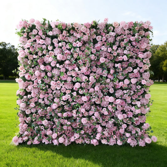 This image features a large, square floral wall outdoors on a lush green lawn. It's densely covered with an array of pink flowers, creating a rich, romantic display. Bathed in sunlight, with trees and a clear sky in the background, the scene exudes a sense of natural beauty, elegance, and charm, perfect for decorative purposes in events or as a picturesque backdrop.
