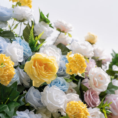 This is a lush, premium artificial flower arrangement, brimming with lifelike blooms in a dreamy pastel palette. It features sky-blue roses, creamy white roses, sunny yellow roses and hydrangeas, blush pink roses, and vibrant green foliage. The dense, realistic design creates a fresh, elegant, romantic focal point, perfect for wedding backdrops, photo booths, bridal showers, and luxury event decor.