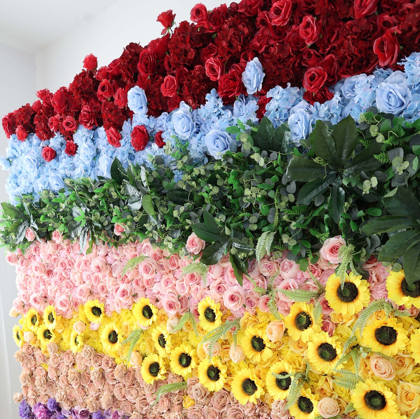 ValarFlowers' floral wall showcases red roses, blue hydrangeas, green eucalyptus, pink roses, yellow sunflowers, and more in a vibrant, colorful display.
