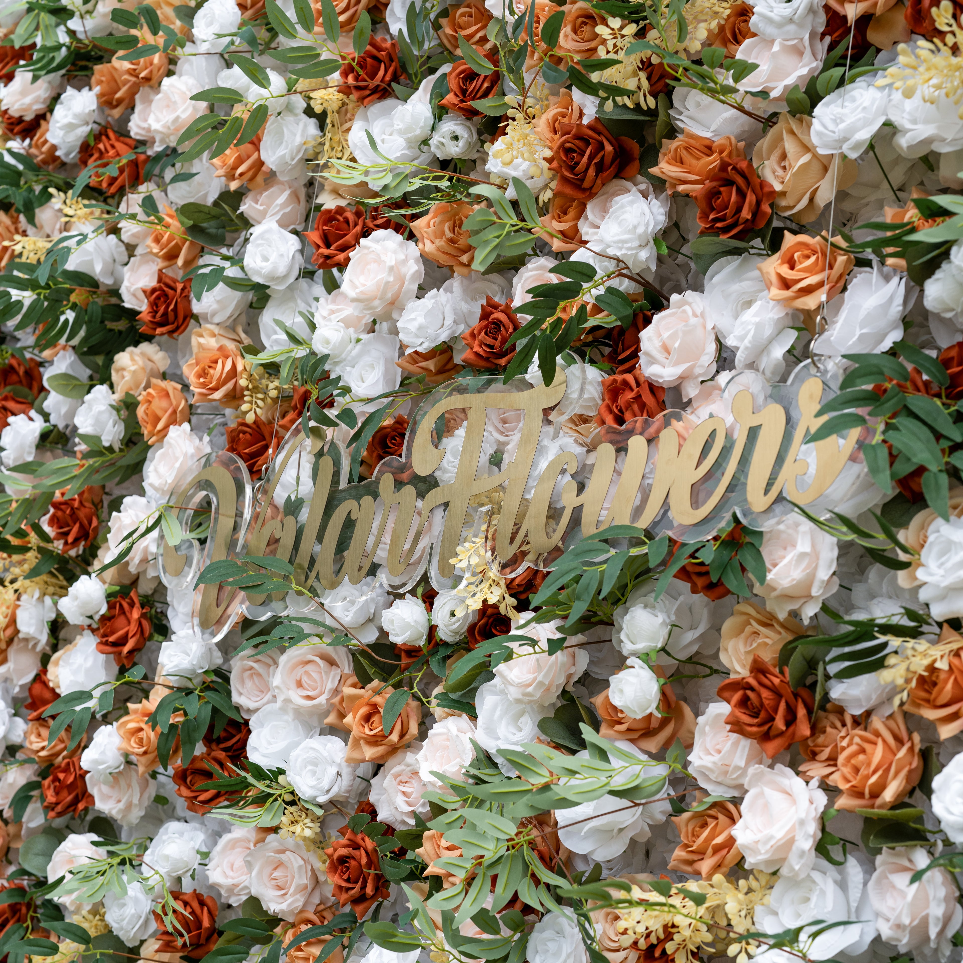 This is a lush, premium artificial flower wall from ValarFlowers, brimming with lifelike blooms in a warm terracotta and cream palette. It features burnt orange roses, creamy white peonies, blush pink roses, and vibrant green foliage, with the brand’s elegant gold script logo at the center. This dense, realistic, reusable arrangement creates a timeless, romantic focal point, perfect for rustic weddings, fall events, photo booths, and luxury event decor.