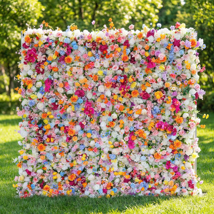 This vibrant flower wall from Valar Flowers is a dense, joyful tapestry of blooms in every hue—roses, daisies, hydrangeas, and delicate sprigs—creating a lush, rainbow-like backdrop. Set against a sunlit lawn and greenery, it evokes a playful, celebratory atmosphere ideal for weddings, photo booths, or lively events.