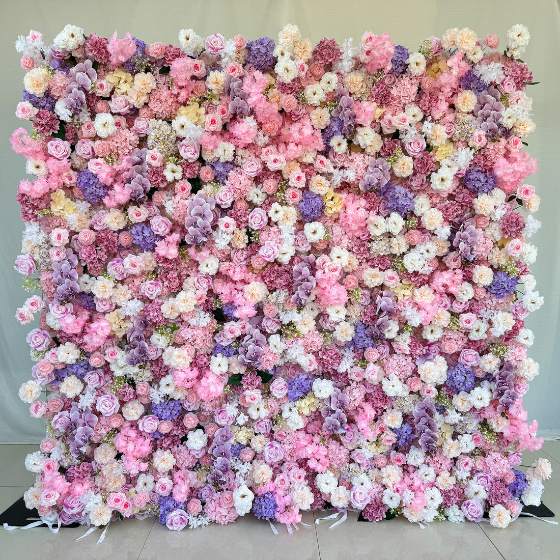 This photo from ValarFlowers showcases a large, dreamy floral backdrop. It is densely covered with an assortment of roses in soft pink, white, and hints of purple. Hydrangeas in shades of purple and pink add fullness, along with delicate carnations in white and light pink. Small white flowers and green foliage complete the arrangement. Ideal for weddings, bridal showers, or romantic events, it exudes elegance and charm. 
