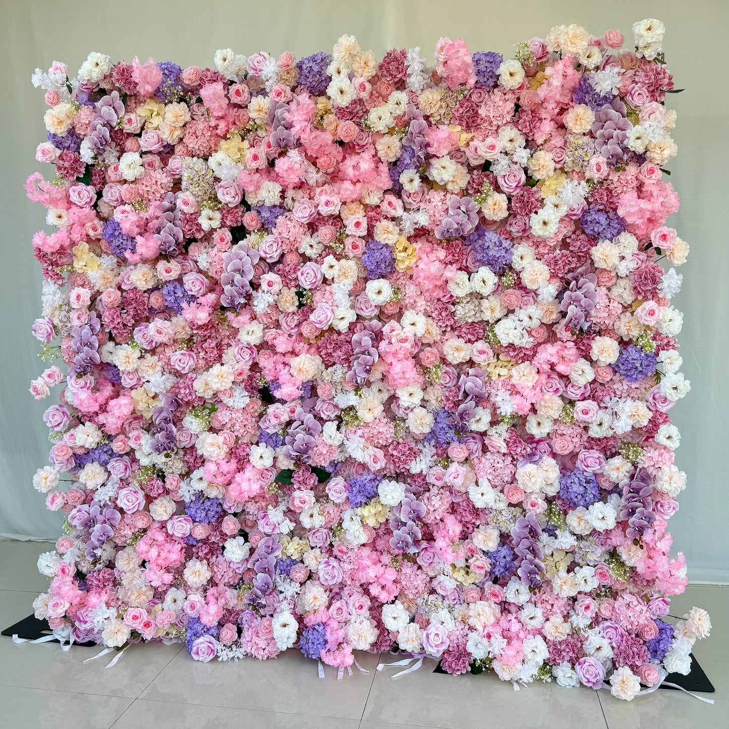 This photo from ValarFlowers showcases a large, enchanting floral backdrop. It is densely adorned with roses in soft pink, white, and peach hues, hydrangeas in shades of purple and pink, and delicate white flowers. Purple orchids add an elegant touch. Ideal for weddings, bridal showers, or romantic events, this dreamy and colorful arrangement exudes charm and sophistication, creating a visually stunning focal point. 