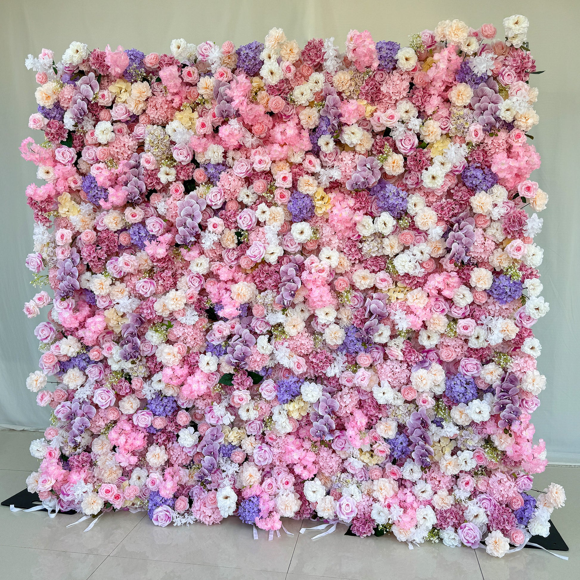This photo from ValarFlowers showcases a large, enchanting floral backdrop. It is densely adorned with roses in soft pink, white, and peach hues, hydrangeas in shades of purple and pink, and delicate white flowers. Purple orchids add an elegant touch. Ideal for weddings, bridal showers, or romantic events, this dreamy and colorful arrangement exudes charm and sophistication, creating a visually stunning focal point. 