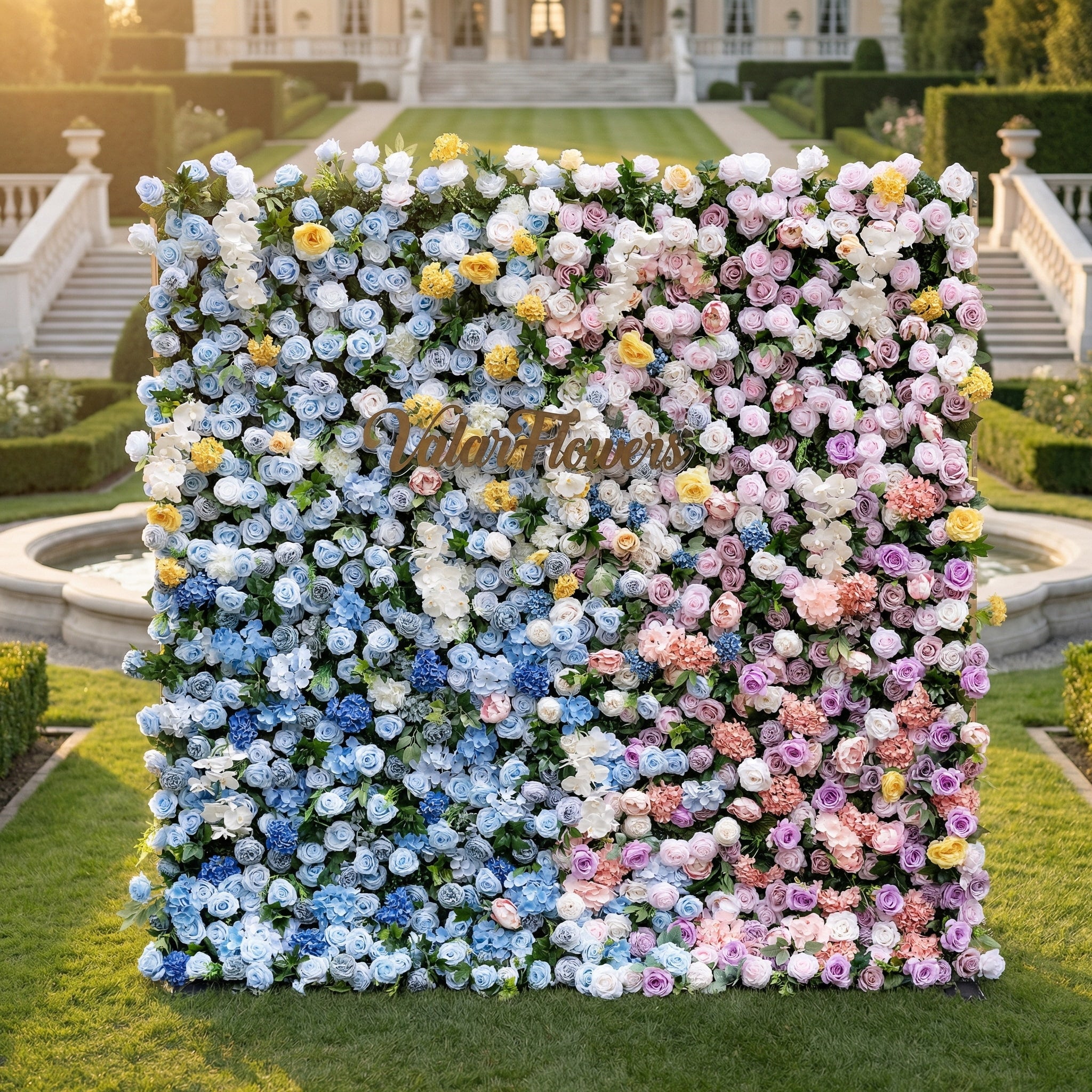 This is ValarFlowers’ premium gradient artificial flower wall backdrop, set against a luxurious European-style garden with a grand staircase and fountain. It features a seamless color transition from sky-blue delphiniums at the base to creamy white roses, sunny yellow poppies, blush pink peonies, and lavender roses at the top. This lifelike, reusable floral arrangement creates an elegant, romantic focal point ideal for weddings, photo booths, bridal showers, and luxury event decor.
