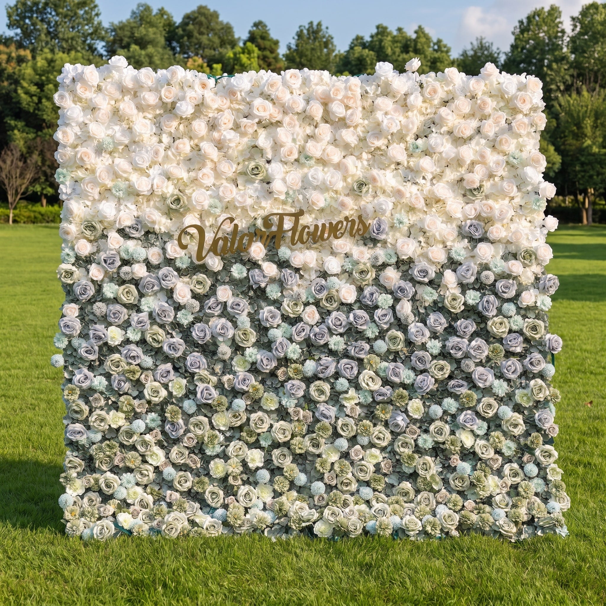 This elegant artificial flower wall by Valar Flowers features a soft gradient from blush pink and ivory roses at the top to muted blue, sage green, and frosty tones below. Set in a sunlit outdoor garden, its dense, layered blooms create a dreamy, romantic aesthetic. Maintenance-free and reusable, this versatile backdrop is ideal for weddings, photo booths, and luxury events, offering a sophisticated, natural-inspired look perfect for professional styling and brand activations.