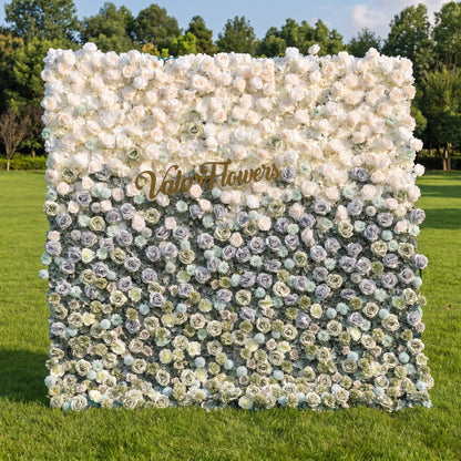 This elegant artificial flower wall by Valar Flowers features a soft gradient from blush pink and ivory roses at the top to muted blue, sage green, and frosty tones below. Set in a sunlit outdoor garden, its dense, layered blooms create a dreamy, romantic aesthetic. Maintenance-free and reusable, this versatile backdrop is ideal for weddings, photo booths, and luxury events, offering a sophisticated, natural-inspired look perfect for professional styling and brand activations.