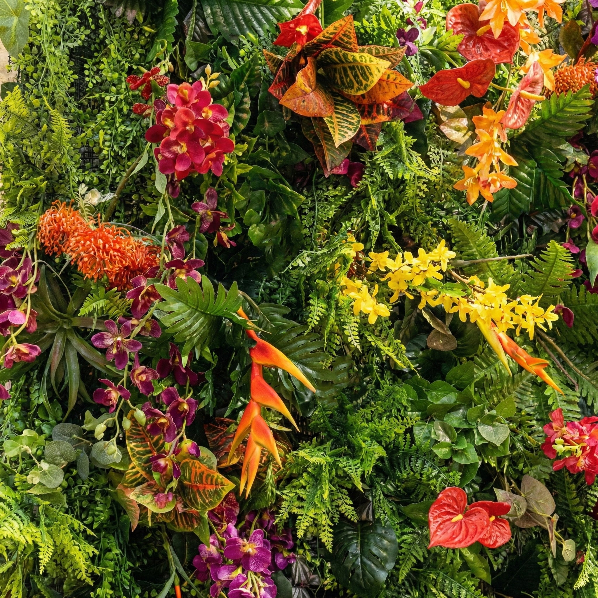 This Valar Flowers tropical flower wall backdrop is a lush, vibrant tapestry of exotic blooms and foliage, featuring bright red anthuriums, deep purple orchids, fiery orange heliconias, sunny yellow sprays, and variegated croton leaves, all layered with ferns and trailing greenery. It creates a bold, jungle-inspired focal point ideal for tropical weddings, summer events, and lively photo opportunities.
