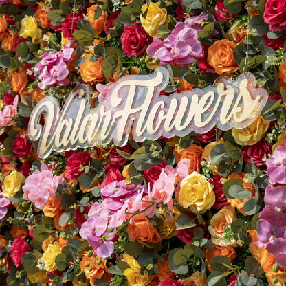 This is a close-up of ValarFlowers’ premium multicolor artificial flower wall, featuring a lush, dense arrangement of lifelike red, orange, yellow roses, pink phalaenopsis orchids, and realistic eucalyptus greenery. Centered is a custom acrylic "ValarFlowers" logo sign. This high-quality, reusable floral backdrop delivers a vibrant, fresh aesthetic, ideal for wedding backdrops, photo booths, summer events, and luxury event decor.