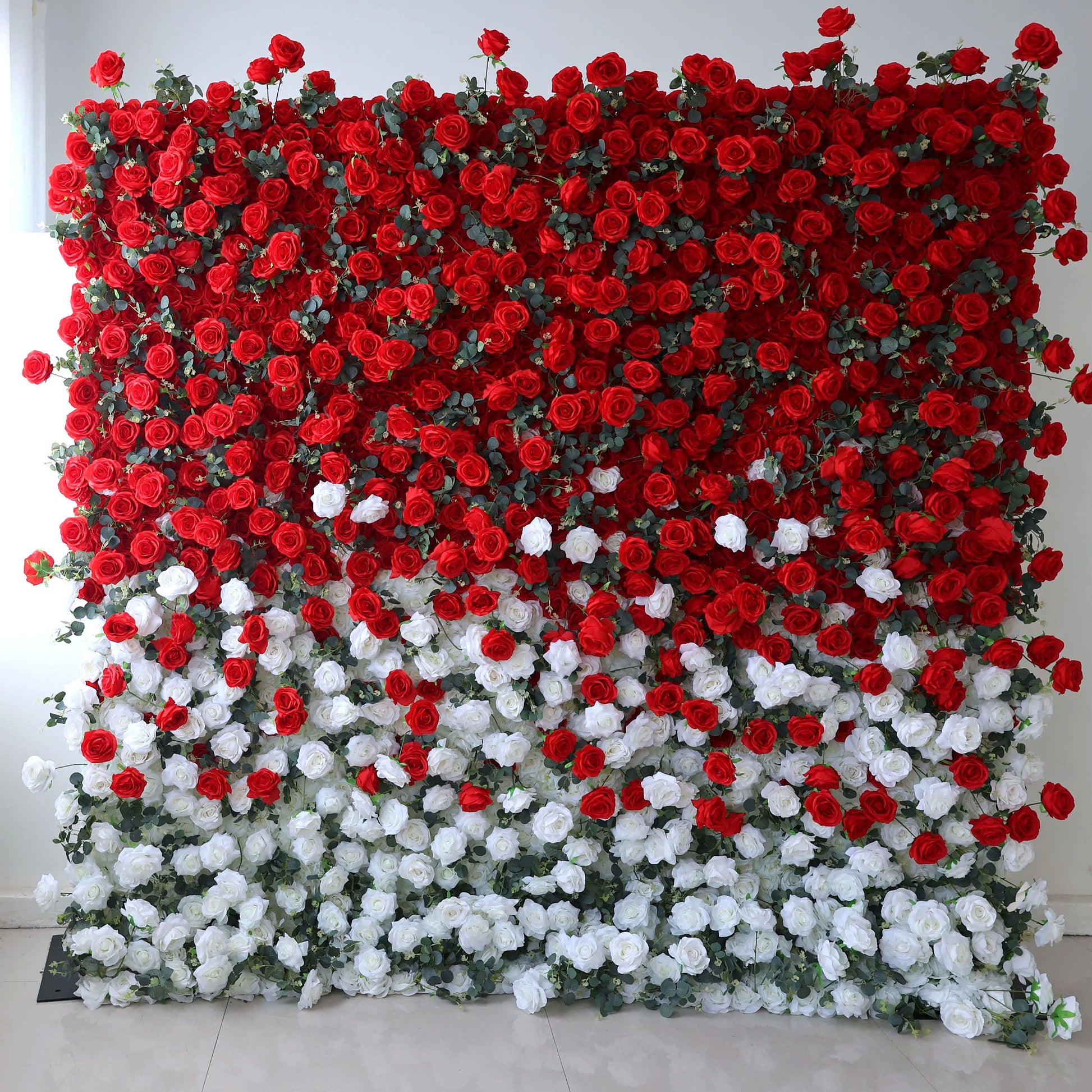 This striking red and white artificial flower wall features a bold gradient design: deep red roses dominate the top, transitioning to crisp white blooms at the bottom, accented with lush green foliage. The dense, layered arrangement creates a dramatic, romantic aesthetic, perfect for weddings, Valentine’s events, and luxury photoshoots. Maintenance-free and reusable, this elegant backdrop adds timeless charm to any special occasion.
