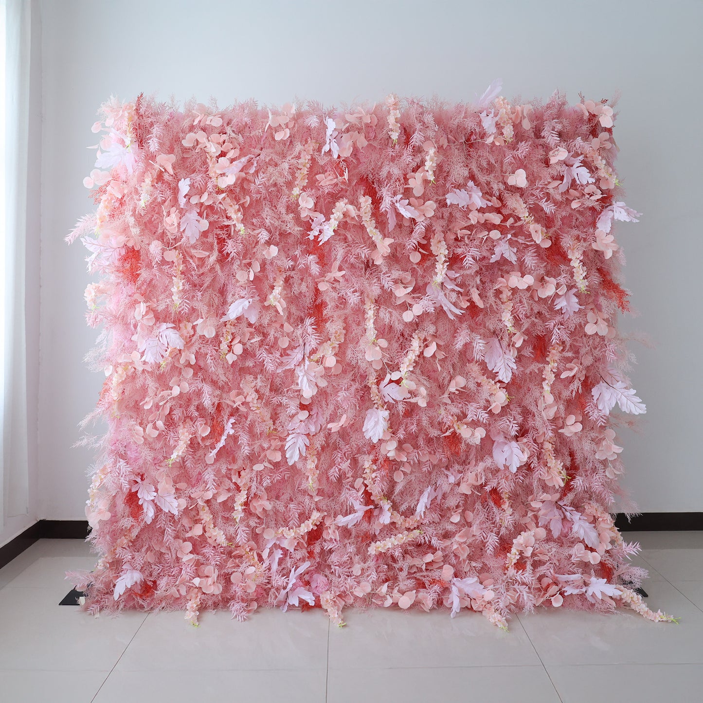 This image showcases a large, dense floral wall indoors. It's covered with an array of delicate pink flowers and foliage, creating a soft and romantic display. Set against a plain wall with a tiled floor, the harmonious blend of various pink hues and intricate floral elements exudes a sense of elegance and gentle charm, perfect for decorative purposes in events or as a striking interior backdrop.
