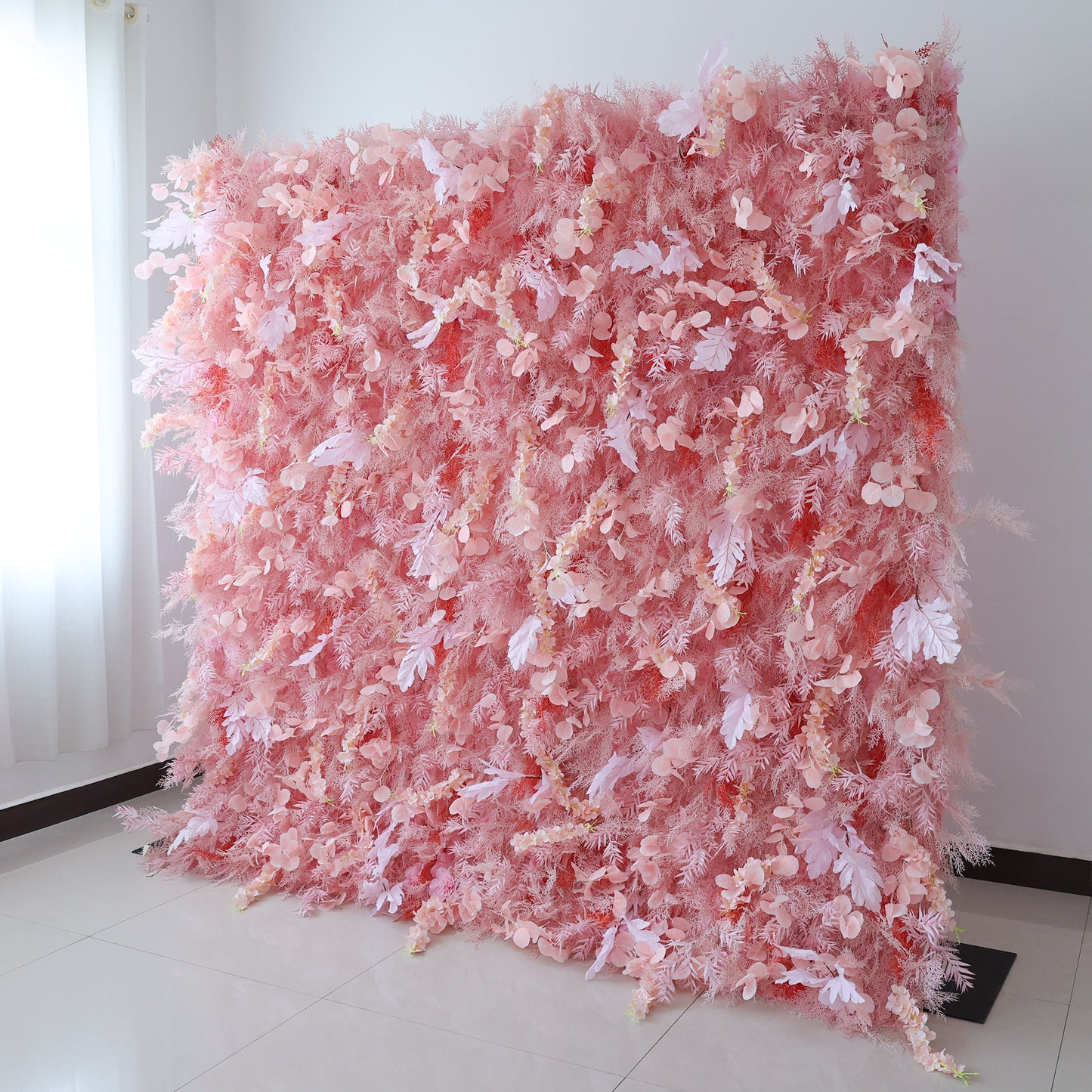 This image showcases a large, dense floral wall indoors. It's covered with an array of delicate pink flowers and foliage, creating a soft and romantic display. Set in a room with white walls and a tiled floor, the harmonious blend of various pink hues and intricate floral elements exudes a sense of elegance and gentle charm, perfect for decorative purposes in events or as a striking interior backdrop.