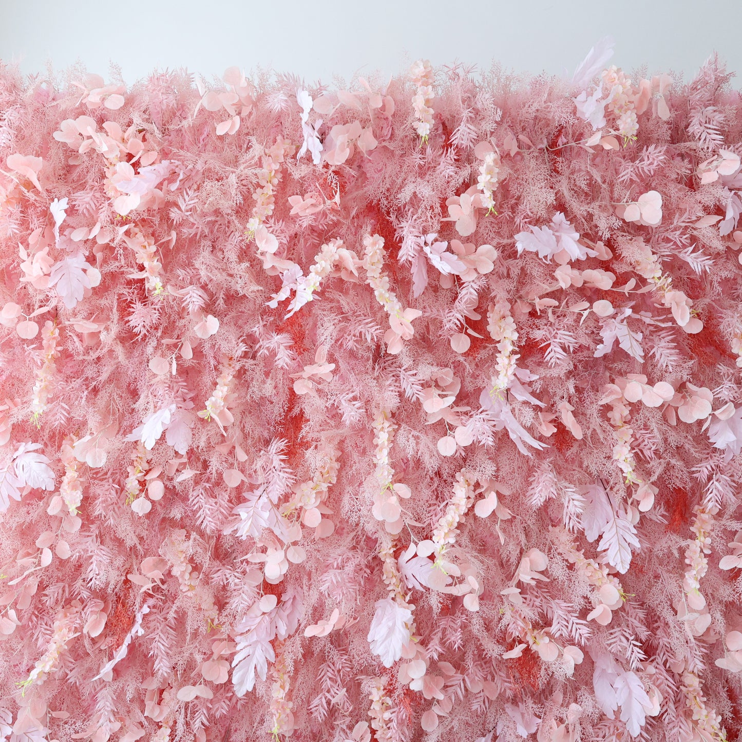 This image showcases a large, dense floral wall indoors. It's covered with an array of delicate pink flowers and foliage, creating a soft and romantic display. The harmonious blend of various pink hues and intricate botanical elements exudes a sense of elegance and gentle charm, perfect for decorative purposes in events or as a striking interior backdrop.