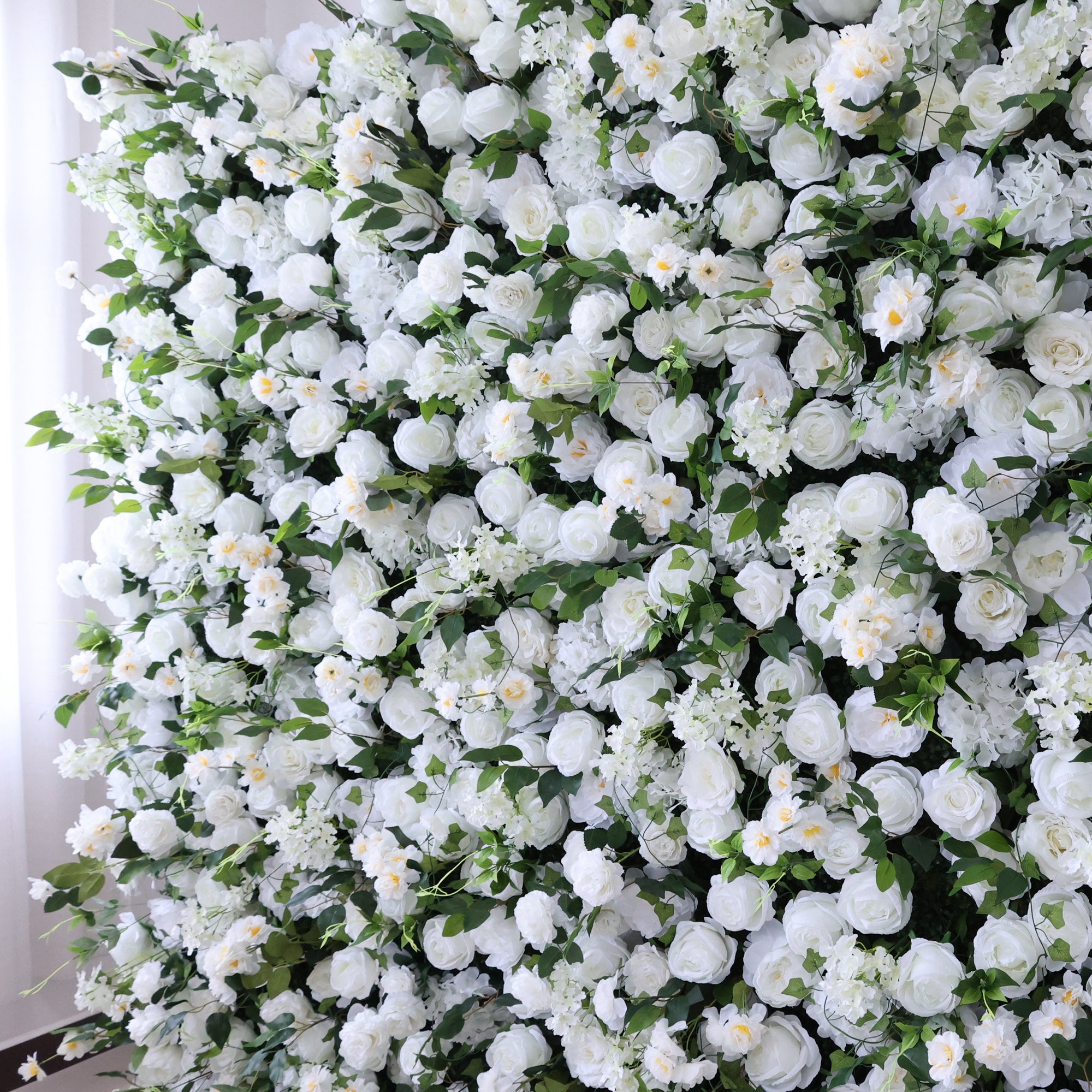 This image displays a dense arrangement of artificial white flowers, mainly roses, interspersed with lush green leaves. The flowers create a rich, elegant tapestry, exuding purity and charm. Perfect for decorative use in events or as an eye - catching interior backdrop, the scene blends pristine white hues and natural - looking foliage to form a visually appealing floral display.