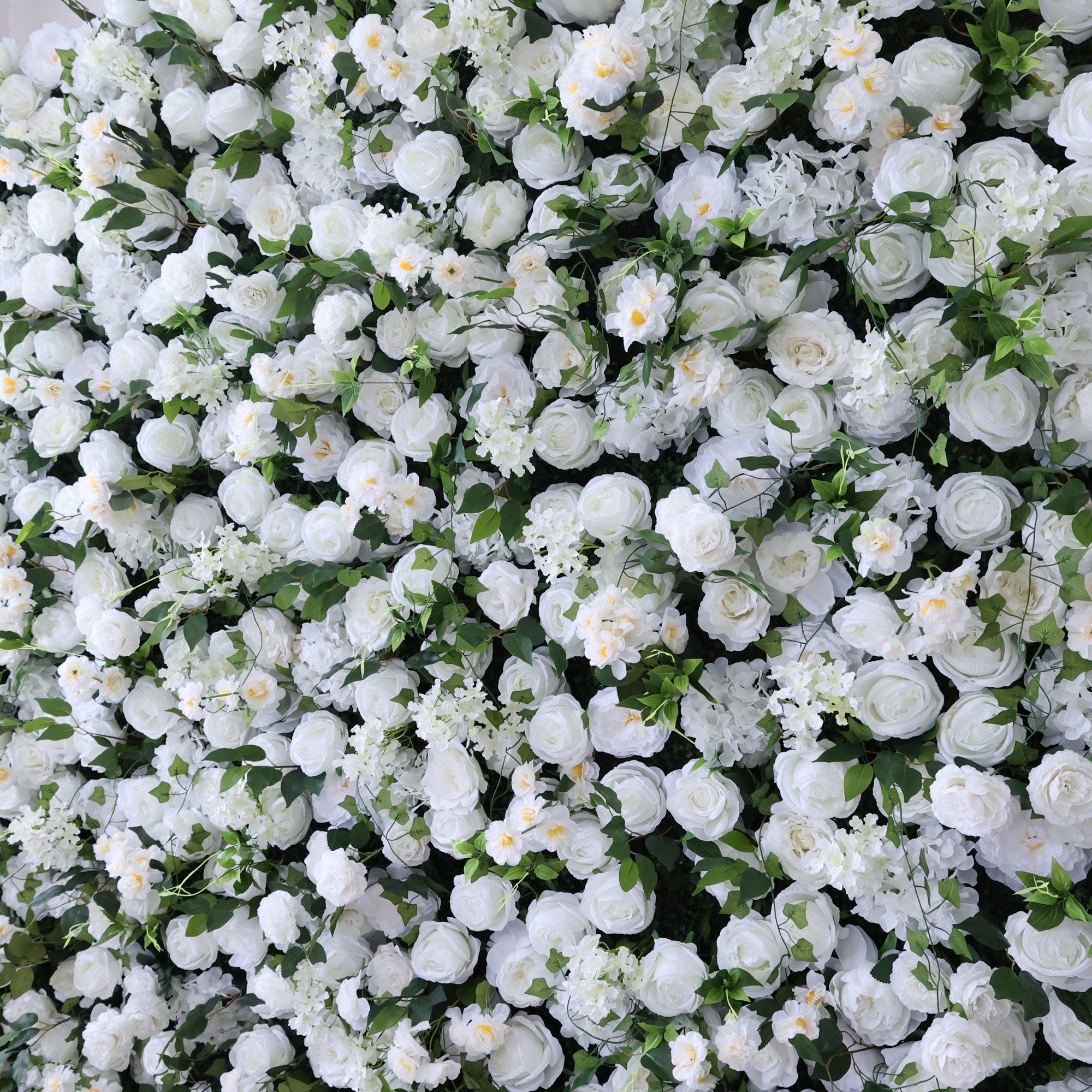 This image presents a dense, vibrant arrangement of artificial white flowers, predominantly roses, interspersed with lush green leaves. The flowers form a rich, elegant tapestry, exuding purity and charm. Ideal for decorative use in events or as an eye - catching interior backdrop, the scene combines pristine white hues and natural - looking foliage to create a visually appealing floral display.
