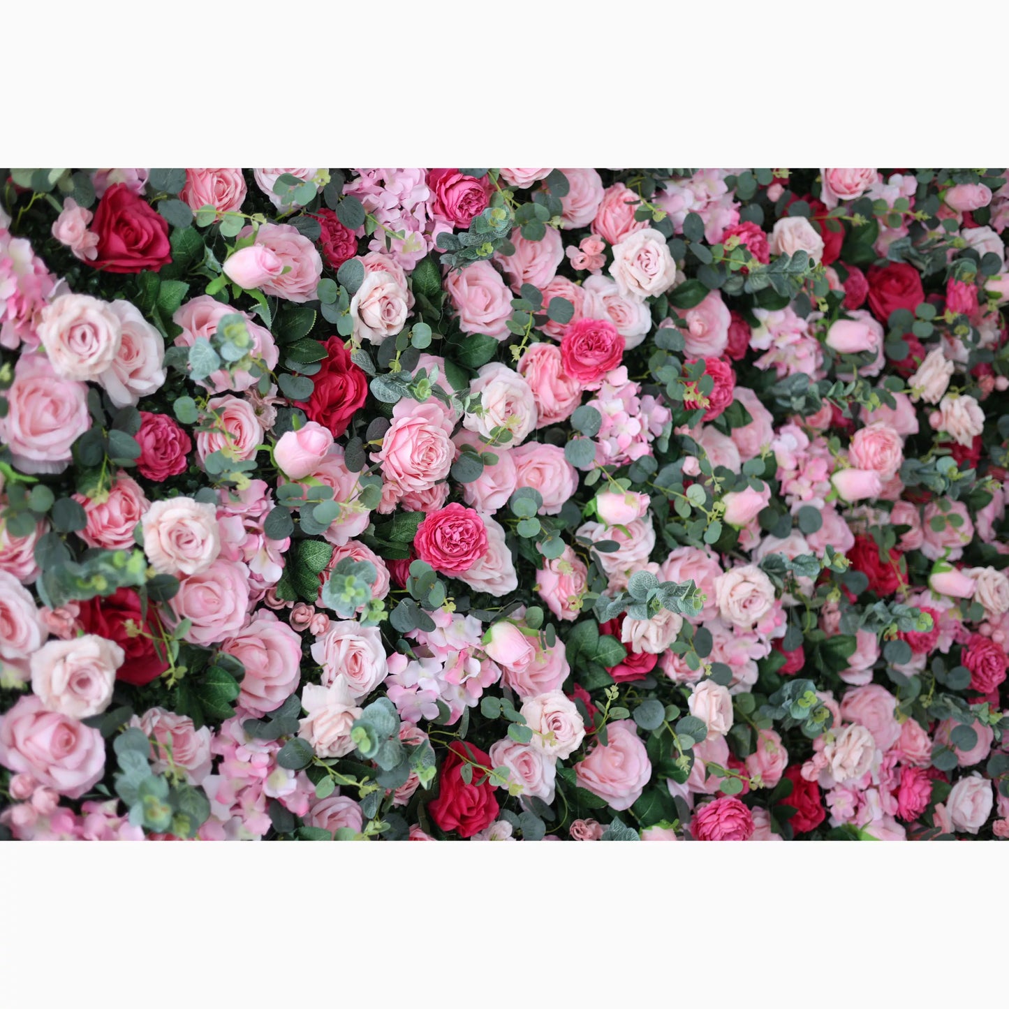 A lush artificial flower wall features a beautiful blend of pink, light pink, and red roses, interspersed with green foliage. The dense, layered blooms create a romantic, vibrant, and visually appealing backdrop, perfect for adding an elegant touch to events or decor. 