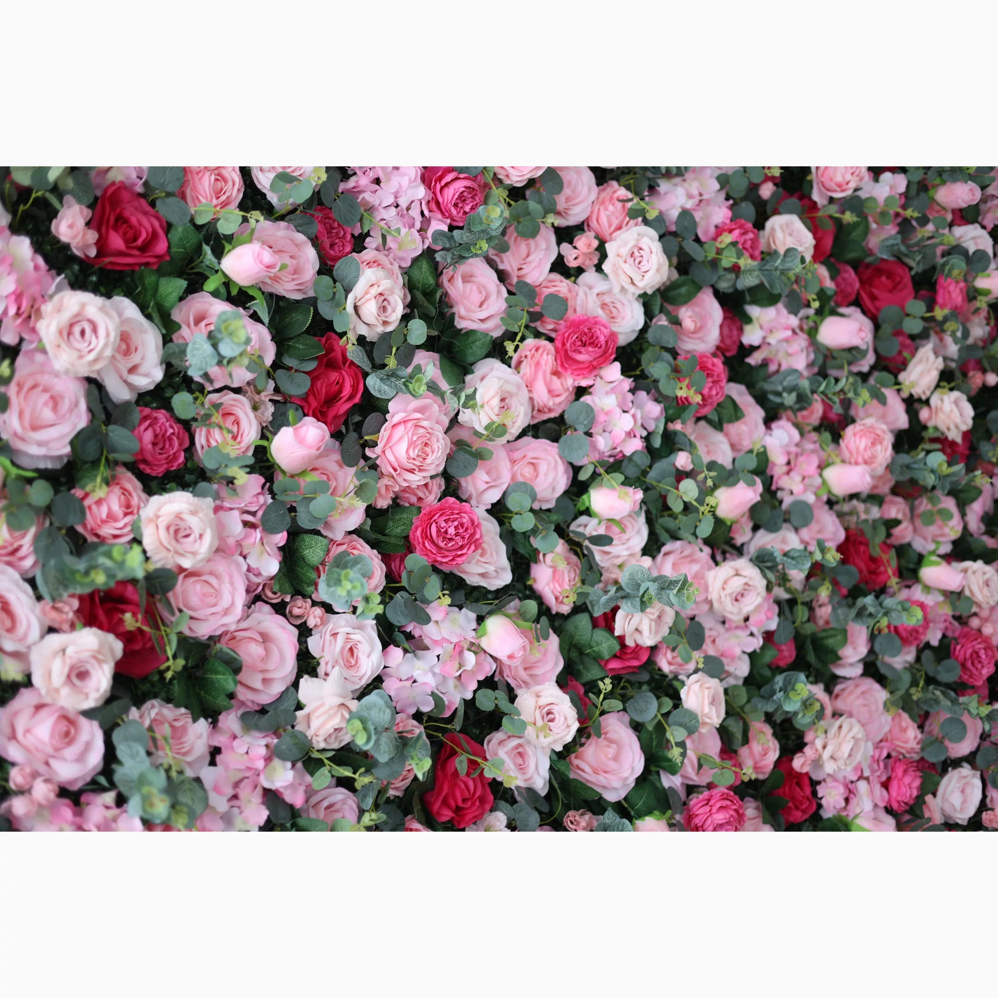 A lush artificial flower wall features a beautiful blend of pink, light pink, and red roses, interspersed with green foliage. The dense, layered blooms create a romantic, vibrant, and visually appealing backdrop, perfect for adding an elegant touch to events or decor. 