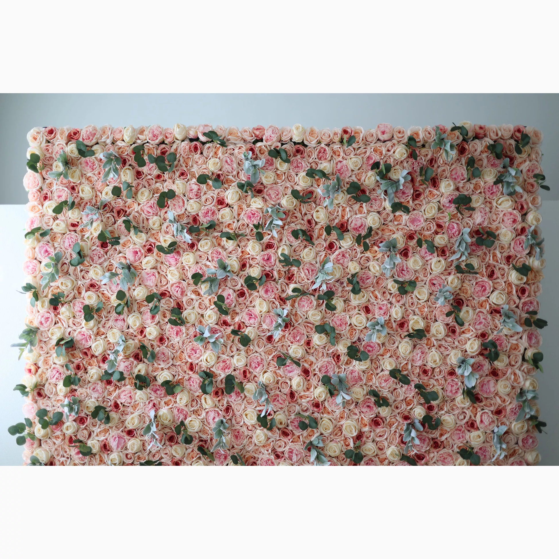 A large artificial flower wall features a dense arrangement of soft - pink and beige roses. Interspersed are green leaves and light - toned foliage, adding texture. The uniform, lush blooms create a sophisticated, romantic backdrop, perfect for adding an elegant touch to events or decor. 