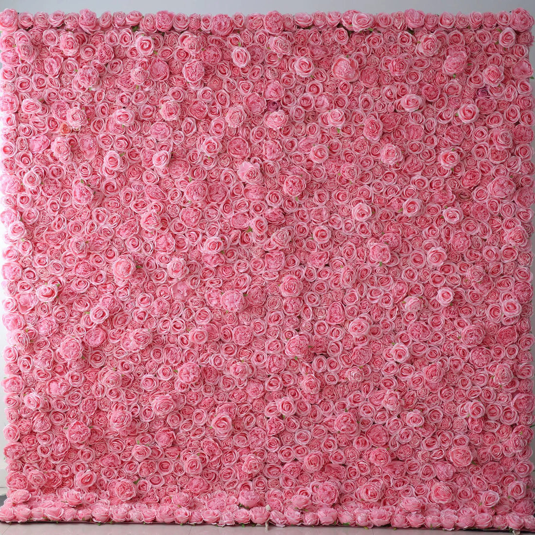 A vast artificial flower wall showcases a dense arrangement of uniform pink roses. Each bloom is tightly clustered, creating a smooth, lush, and romantic texture. The consistent pink hue gives a soft, elegant, and dreamy vibe, perfect for adding a touch of sweetness to decor or event backdrops.