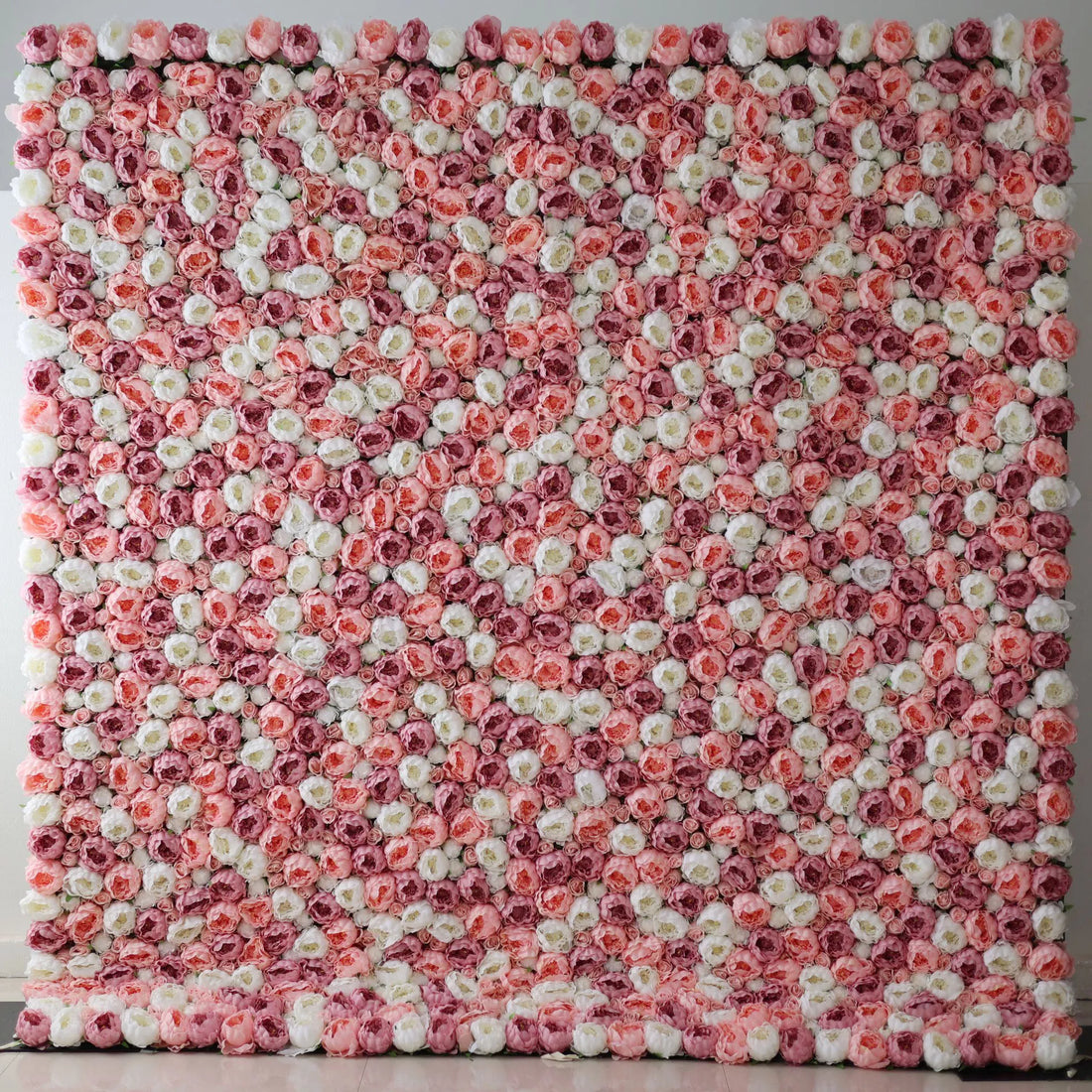 A large artificial flower wall features a mesmerizing pattern of pink, white, and light pink roses. The blooms are densely packed, creating a lush, textured, and visually striking backdrop. The harmonious color blend gives off a romantic, elegant vibe, perfect for adding a decorative touch to events or spaces.