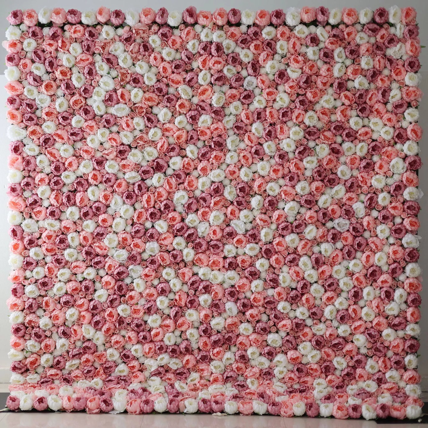 A large artificial flower wall features a mesmerizing pattern of pink, white, and light pink roses. The blooms are densely packed, creating a lush, textured, and visually striking backdrop. The harmonious color blend gives off a romantic, elegant vibe, perfect for adding a decorative touch to events or spaces. 