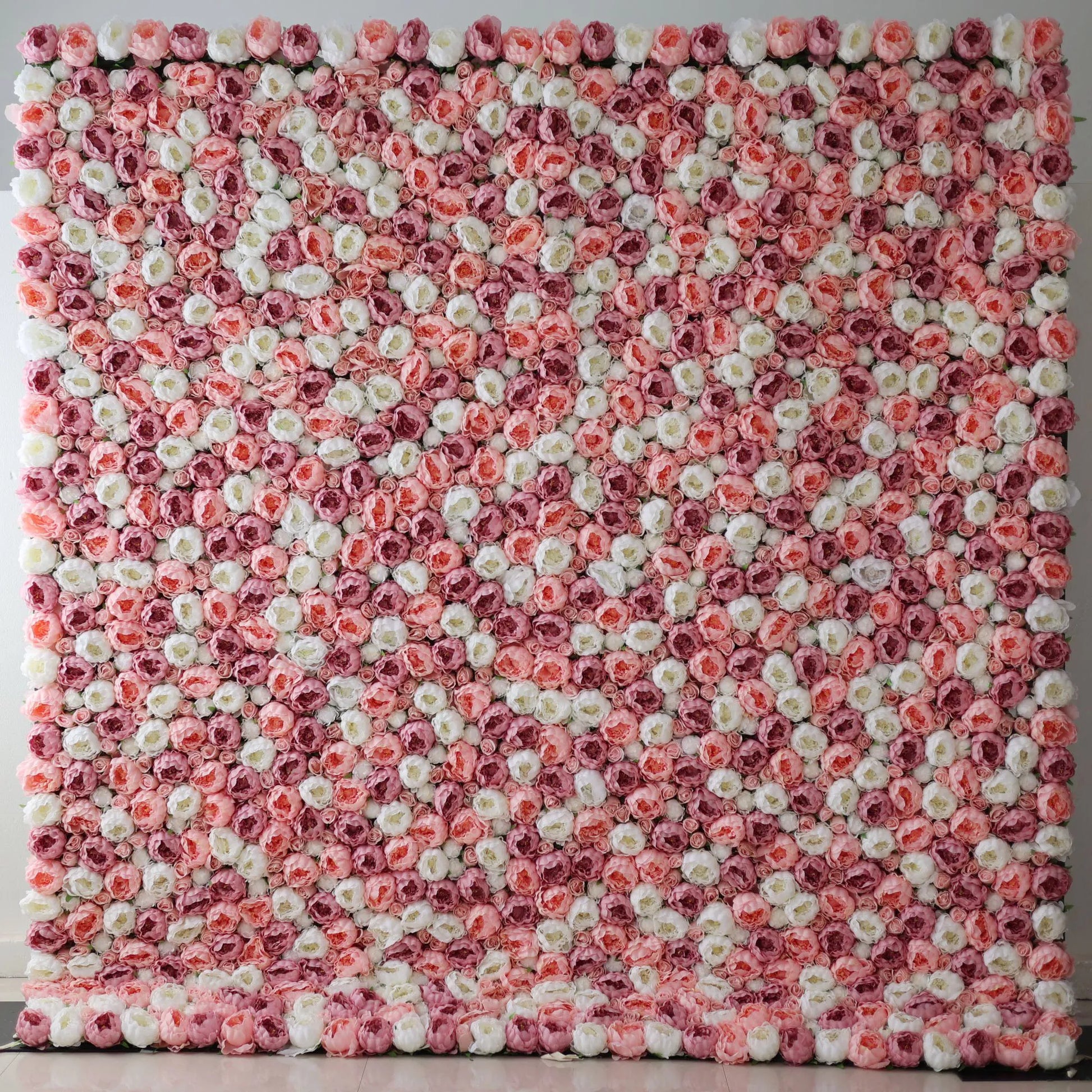 A large artificial flower wall features a mesmerizing pattern of pink, white, and light pink roses. The blooms are densely packed, creating a lush, textured, and visually striking backdrop. The harmonious color blend gives off a romantic, elegant vibe, perfect for adding a decorative touch to events or spaces. 