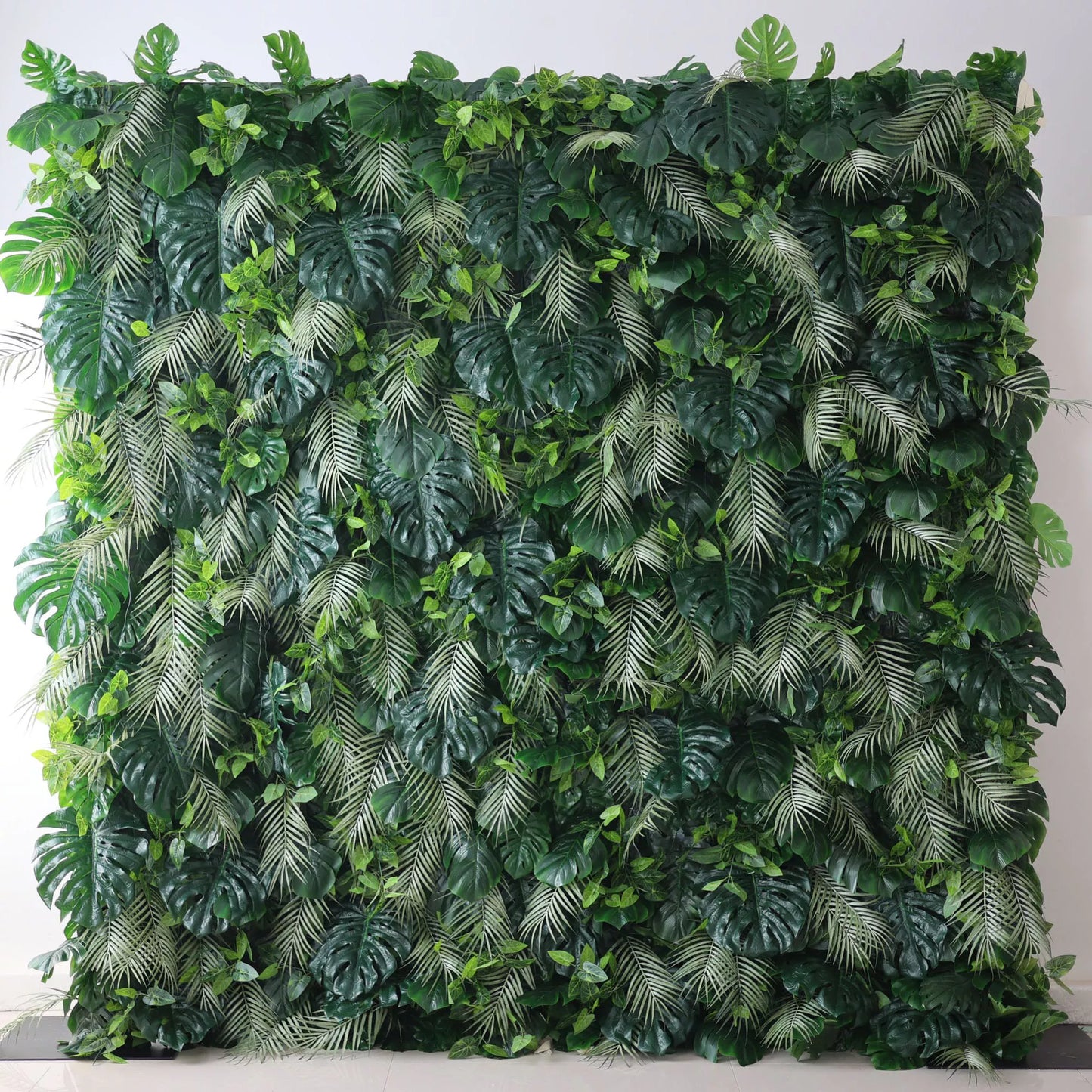 Valar Flowers' Artificial Fabric Green Wall: Tropical Eden. A luxuriant cascade of varied green leaves, meticulously crafted, capturing the heart of a tropical jungle, and radiating verdant serenity. A large artificial greenery wall features a dense mix of lush leaves. Big monstera leaves and delicate fern - like fronds in various shades of green create a vibrant, tropical - inspired texture. It’s a fresh, natural - looking backdrop, perfect for adding an organic touch to decor or events. 