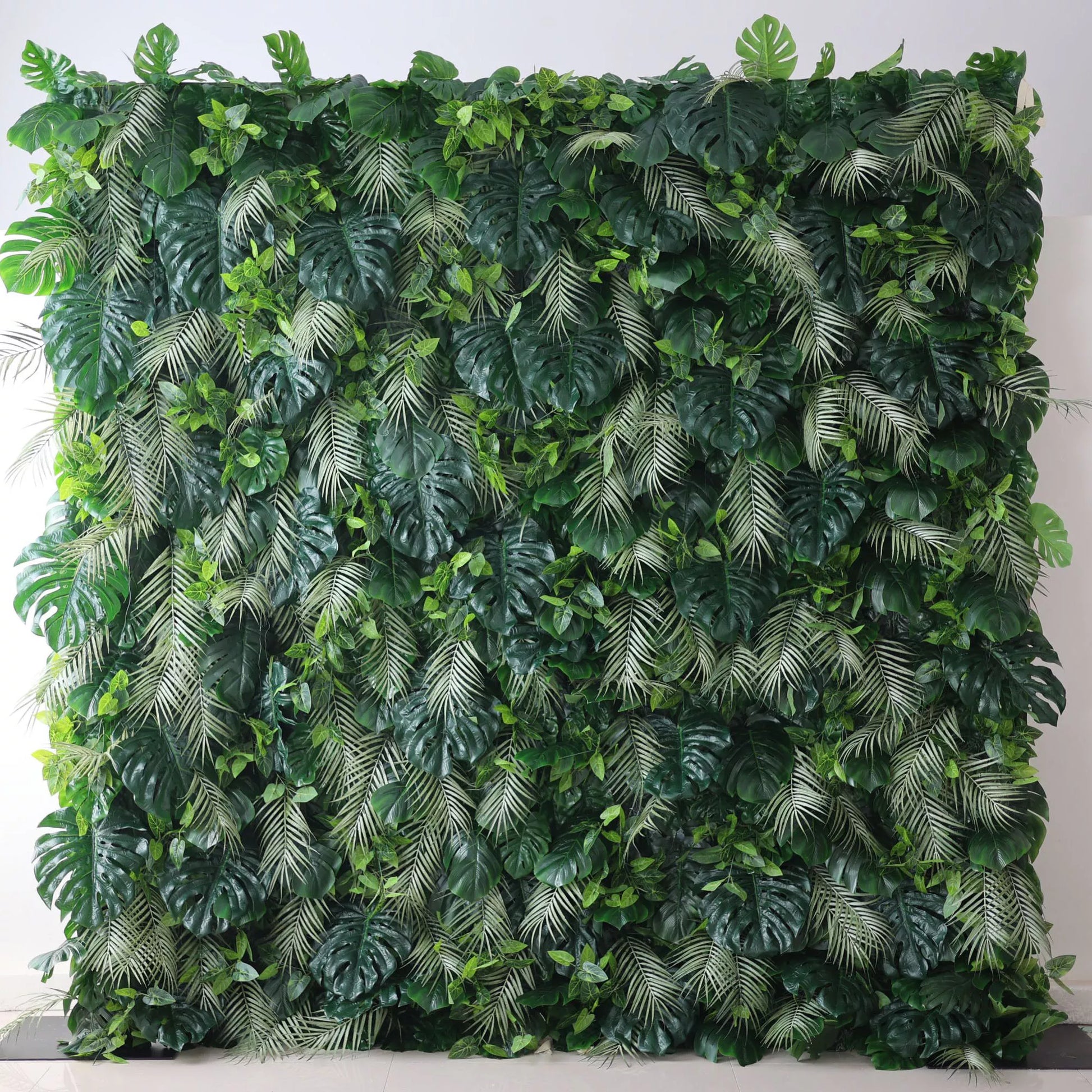 Valar Flowers' Artificial Fabric Green Wall: Tropical Eden. A luxuriant cascade of varied green leaves, meticulously crafted, capturing the heart of a tropical jungle, and radiating verdant serenity. A large artificial greenery wall features a dense mix of lush leaves. Big monstera leaves and delicate fern - like fronds in various shades of green create a vibrant, tropical - inspired texture. It’s a fresh, natural - looking backdrop, perfect for adding an organic touch to decor or events. 