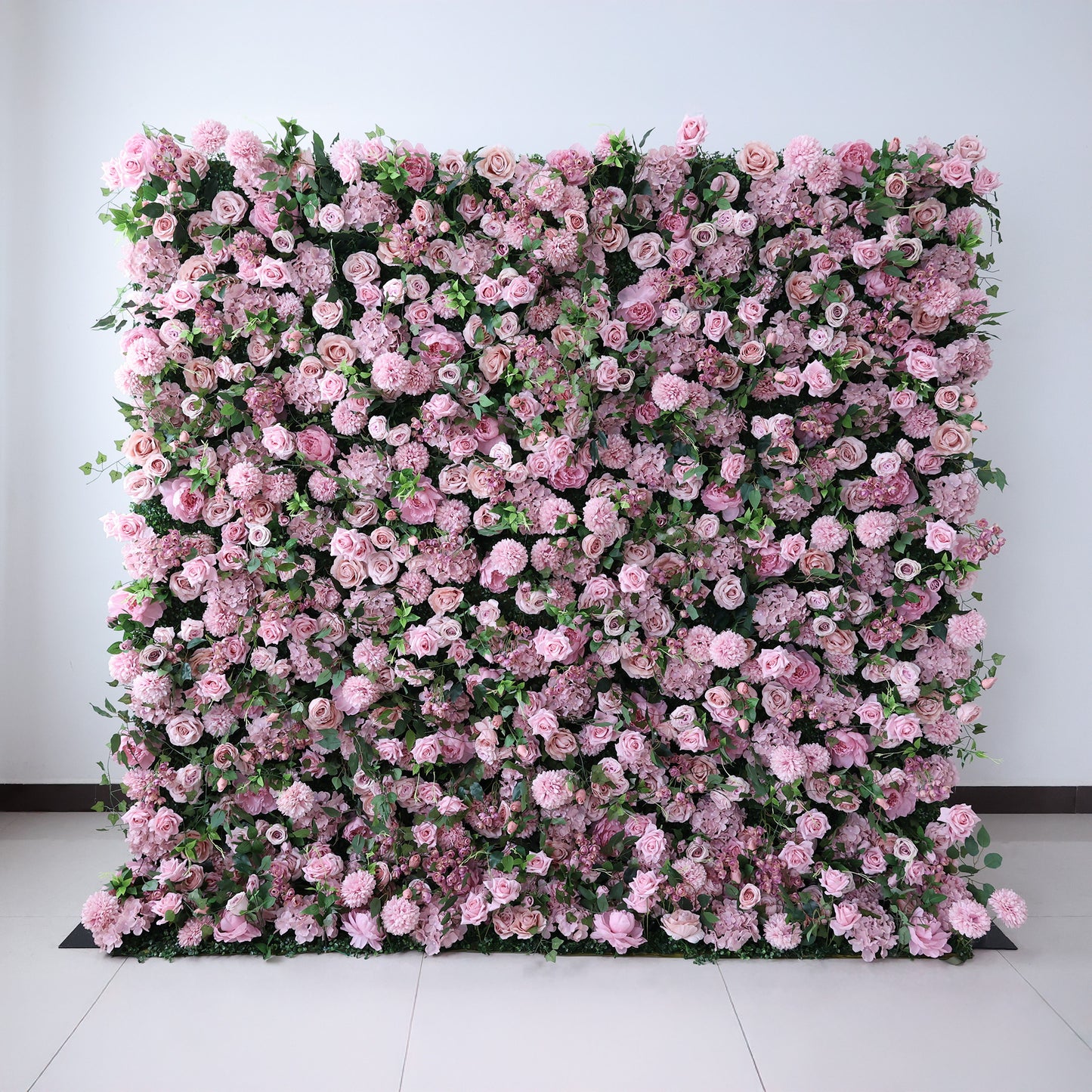 This image showcases a large, square floral wall indoors. It's densely covered with an array of pink flowers, creating a rich, romantic display. Set against a plain wall with a tiled floor, the scene exudes a sense of elegance and charm, perfect for decorative purposes in events or as a striking interior backdrop.
