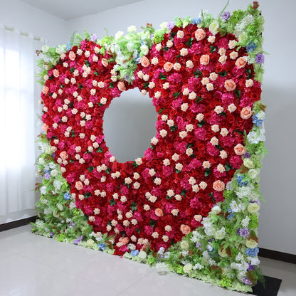 This vibrant indoor floral wall from **Valar Flowers** is a lush, eye-catching tapestry of deep red, blush pink, and creamy white blooms—including roses, peonies, and delicate filler flowers—interwoven with vibrant green foliage and subtle blue and purple accents. The design features a striking circular cutout at its center, creating a dramatic focal point. 