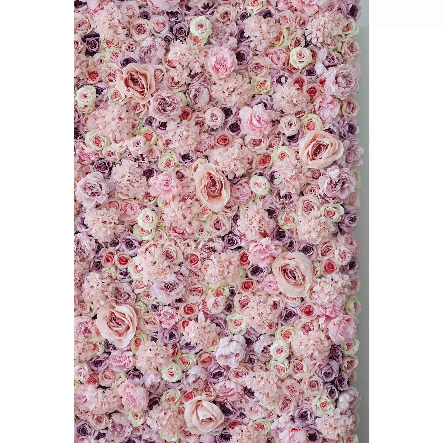 This lush, immersive floral wall is a dense arrangement of artificial blooms in a soft, romantic palette of blush pink, ivory, and subtle lavender. It features large, ruffled roses, delicate peonies, and clustered filler flowers, creating a rich, multi-textured surface. The gentle gradient of pastel tones and varied bloom sizes evoke a dreamy, timeless elegance, making it ideal for wedding backdrops, photo booths, or upscale interiors seeking a feminine, romantic focal point.