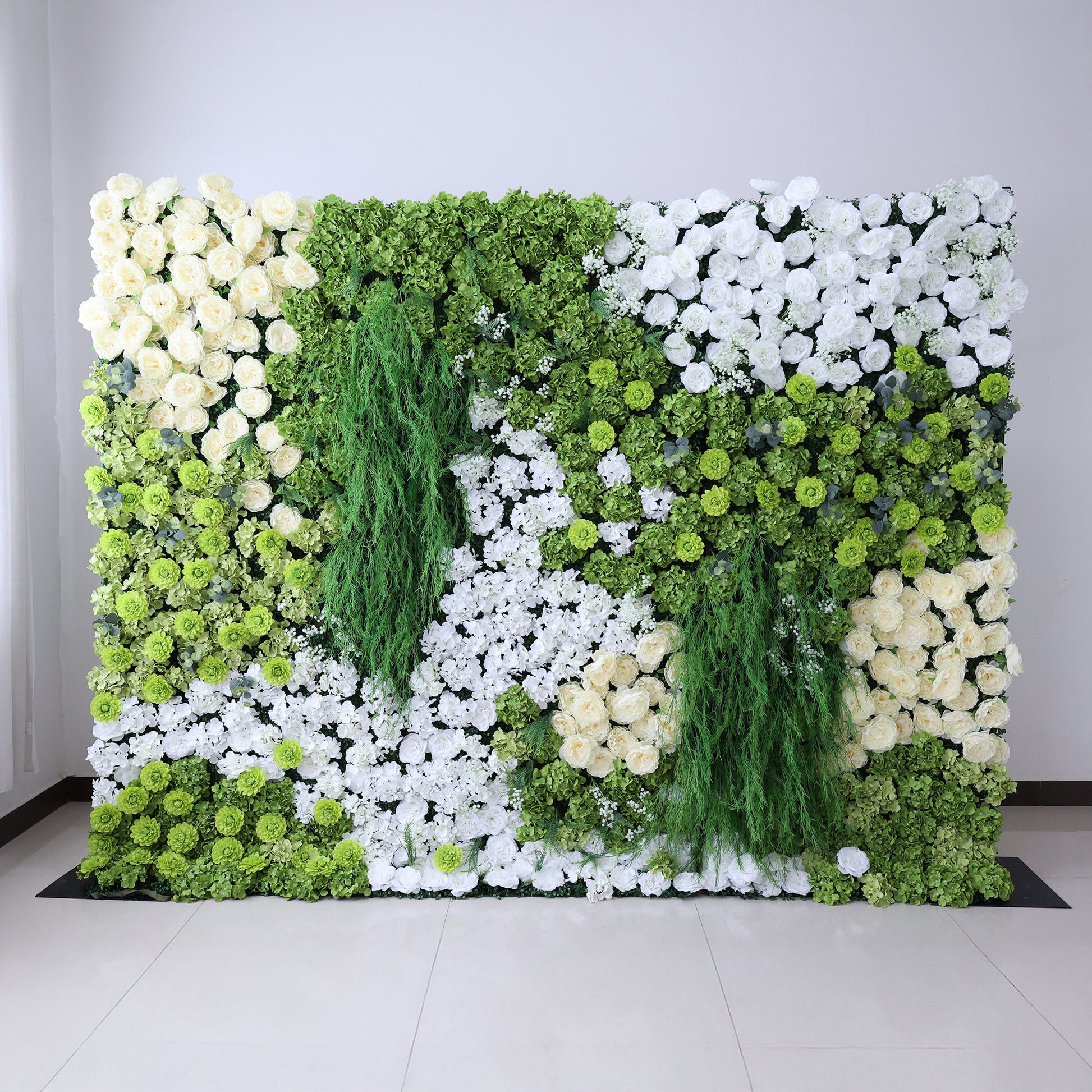 This image features a large, square floral wall indoors. It combines various white flowers with abundant green foliage and trailing vines, creating a vibrant, natural, and refreshing display. Set against a plain white wall with a shiny tiled floor, the scene exudes a sense of vitality, harmony, and elegance, perfect for decorative purposes in events or as a striking interior backdrop, blending artificial artistry with a touch of nature's charm.