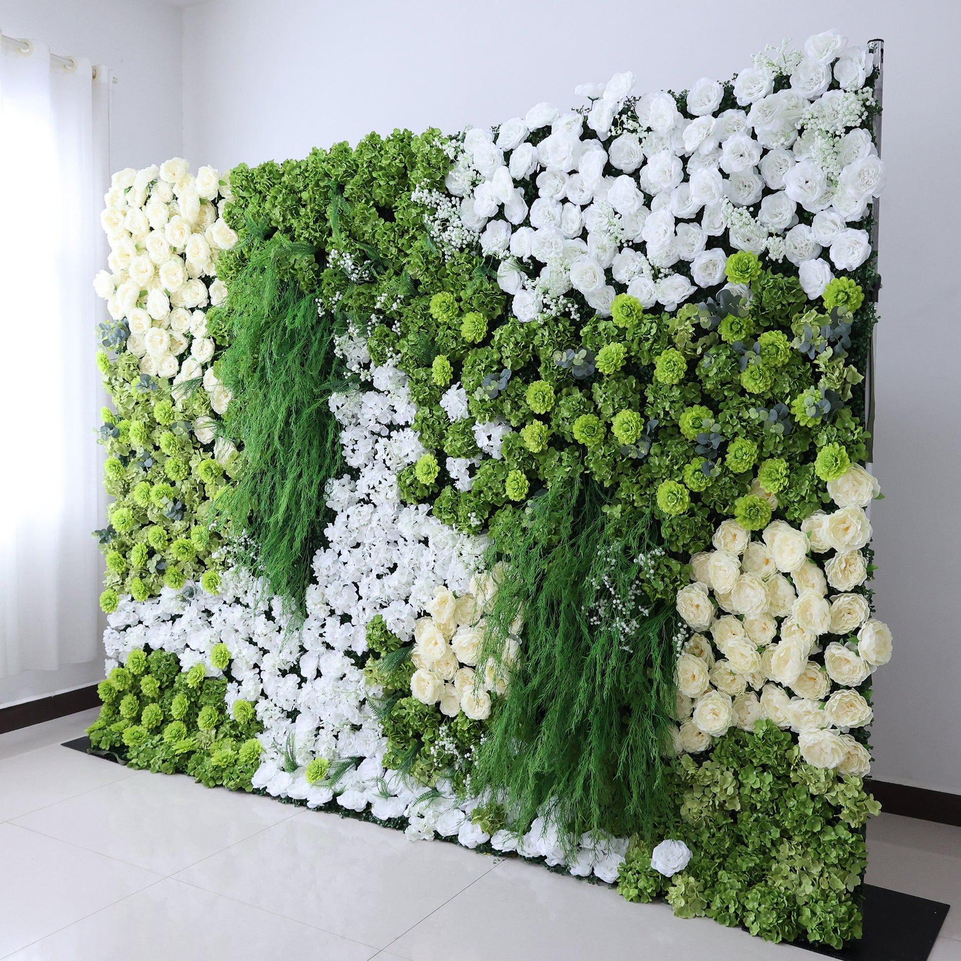 This image features a large, square floral wall indoors. It combines various white flowers with abundant green foliage and trailing vines, creating a vibrant, natural, and refreshing display. Set against a plain white wall with a shiny tiled floor, the scene exudes a sense of vitality, harmony, and elegance, perfect for decorative purposes in events or as a striking interior backdrop, blending artificial artistry with a touch of nature's charm.