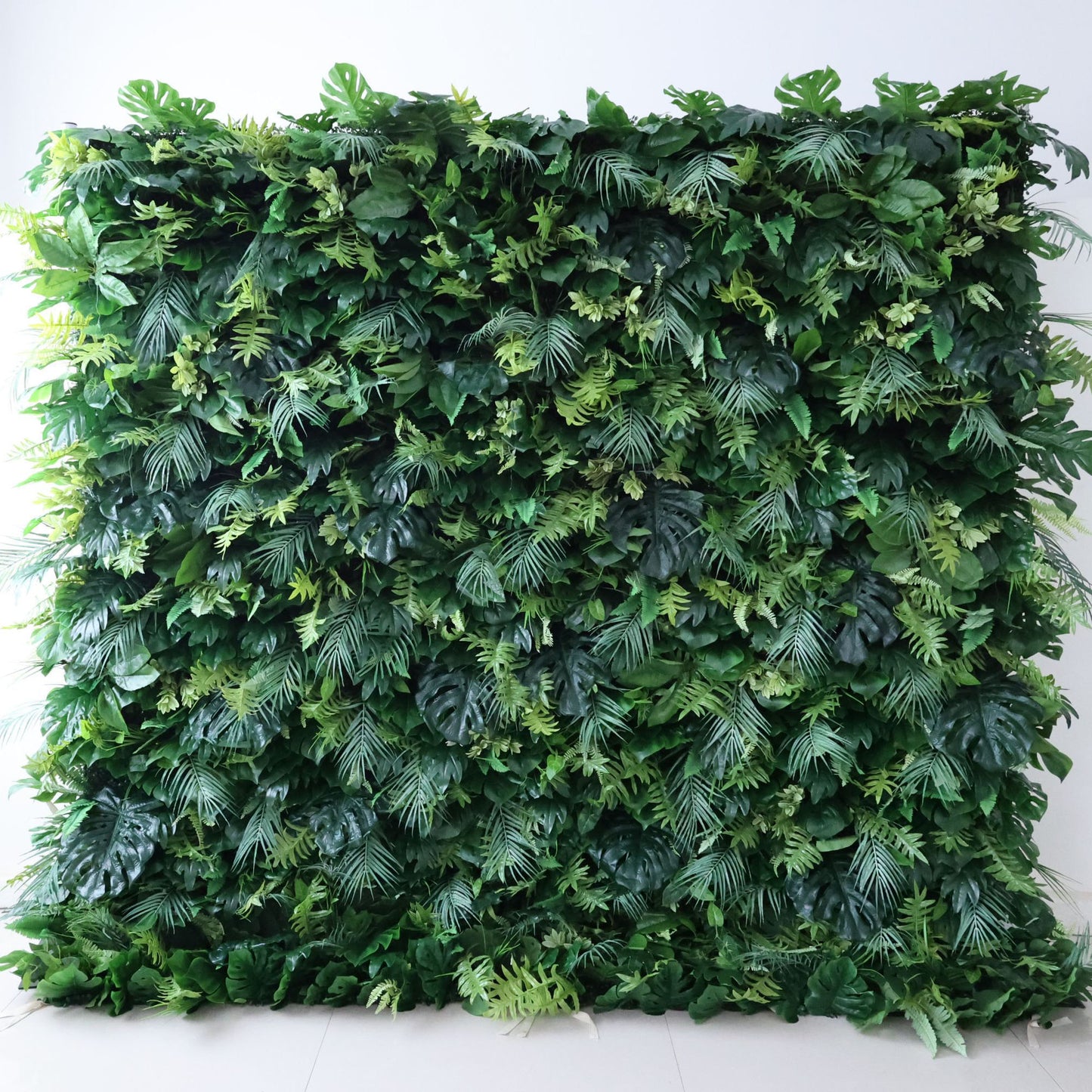 This Valar Flowers greenery wall is a dense, textured panel of varied foliage—including monstera leaves, delicate ferns, and tropical fronds—in layered shades of green (deep forest, soft lime). Set against a plain light backdrop, the lush mix creates a vibrant, organic surface. Though not a floral arch, this piece embodies Valar’s nature-focused styling: ideal as an event backdrop or decor accent, blending rich texture with a fresh, versatile aesthetic.