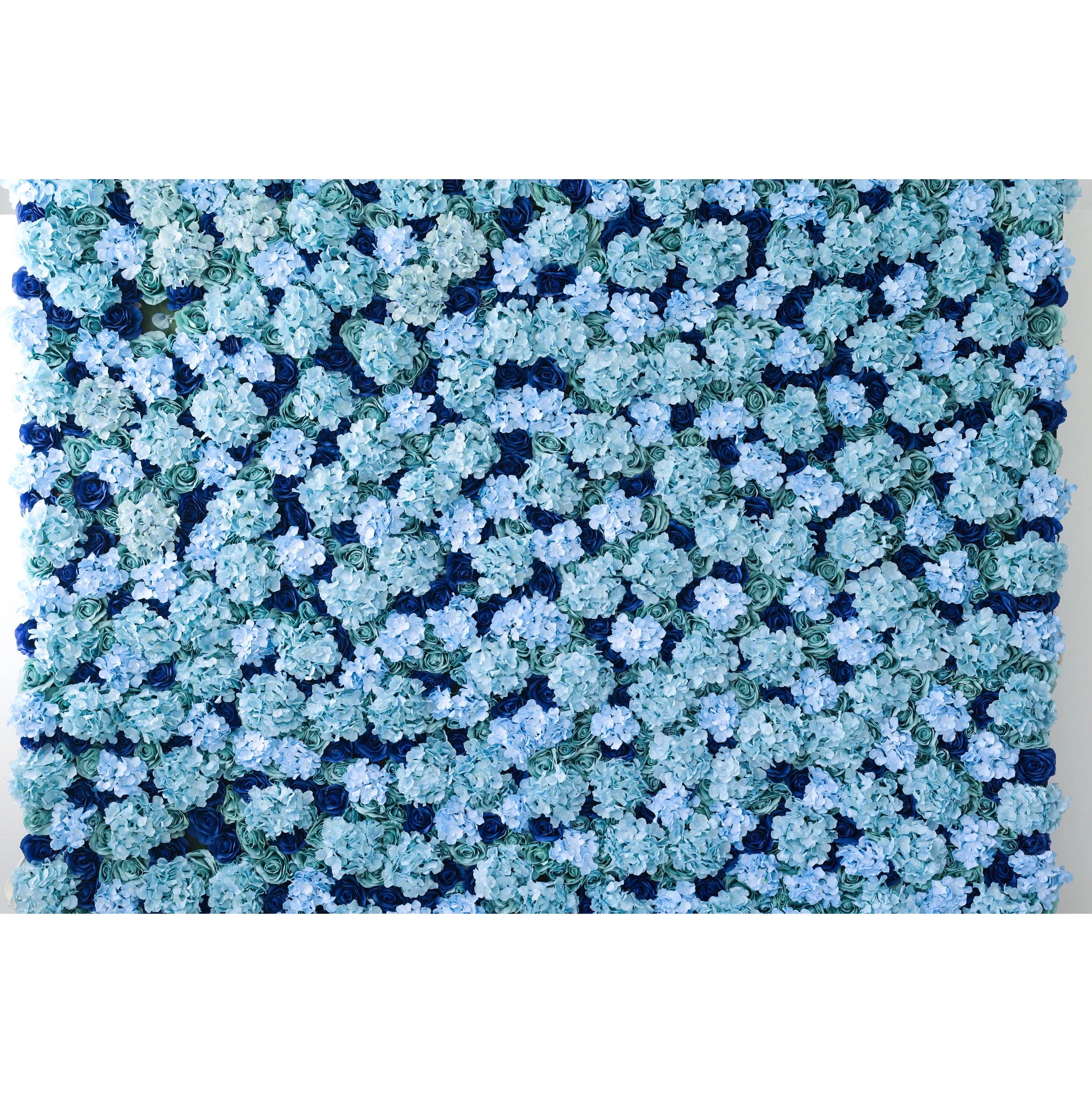 A large artificial flower wall showcases dense blue hydrangeas in varying shades, interspersed with green roses and dark blue blossoms. A small blue circle stands out in the center, adding a unique focal point. The rich, harmonious colors create an elegant, serene backdrop, perfect for refined decor or events. 