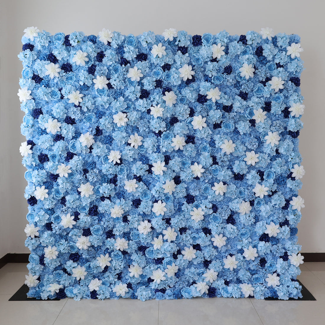A large artificial flower wall features a stunning arrangement of blue hydrangeas, white blooms, and dark blue blossoms. The dense, uniform pattern creates a serene, elegant backdrop, perfect for events or decorative displays, evoking a calm and sophisticated ambiance.