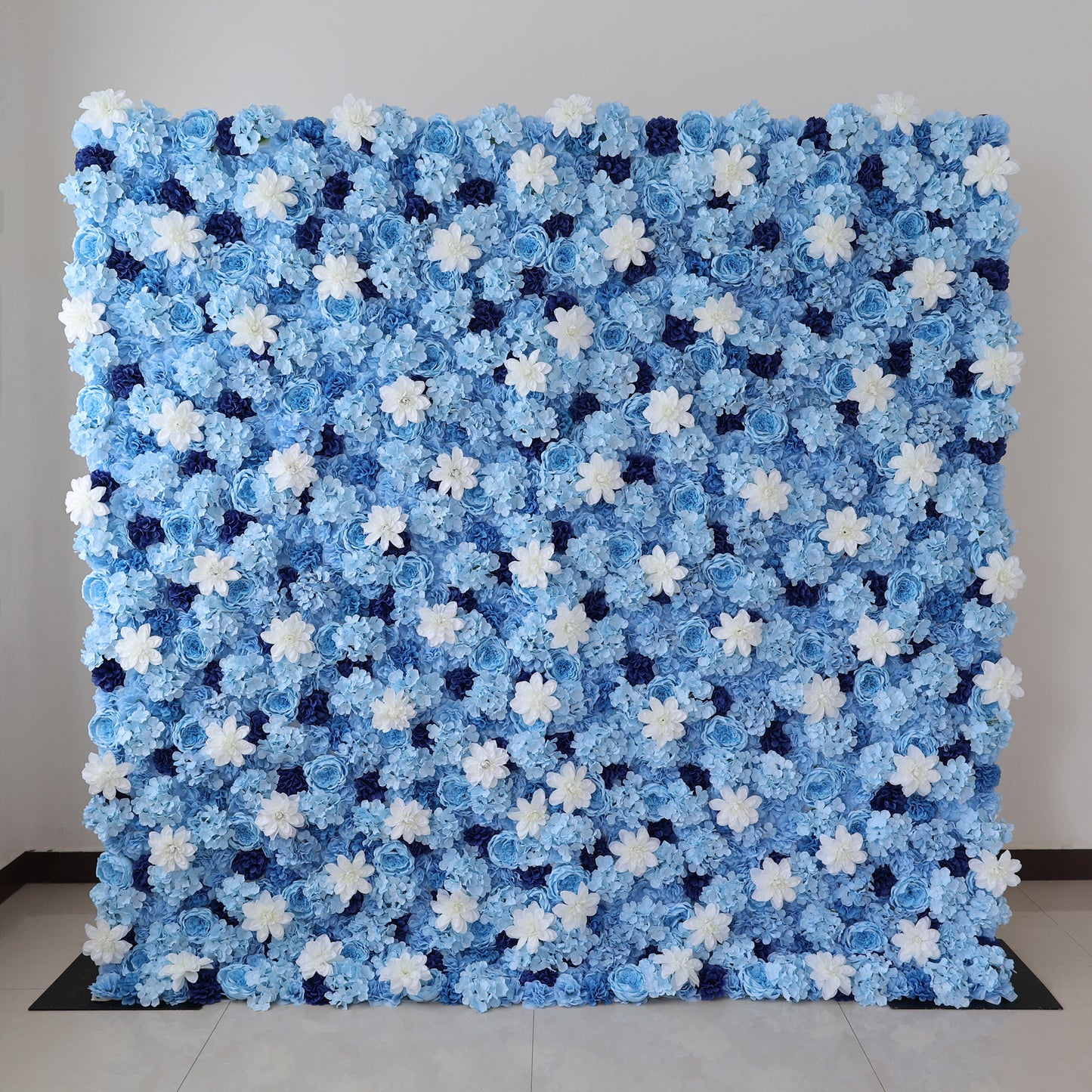 A large artificial flower wall features a stunning arrangement of blue hydrangeas, white blooms, and dark blue blossoms. The dense, uniform pattern creates a serene, elegant backdrop, perfect for events or decorative displays, evoking a calm and sophisticated ambiance. 