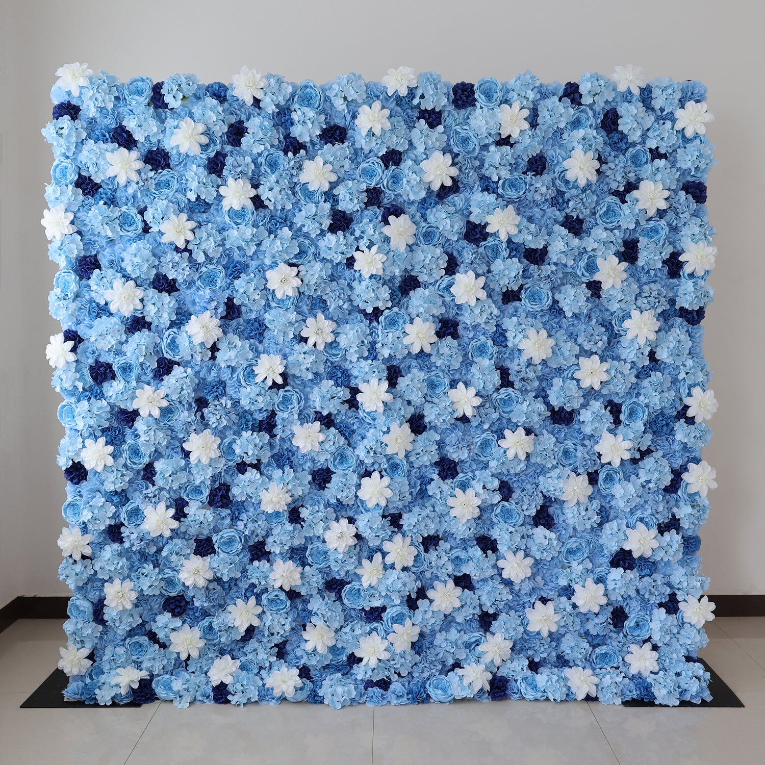 A large artificial flower wall features a stunning arrangement of blue hydrangeas, white blooms, and dark blue blossoms. The dense, uniform pattern creates a serene, elegant backdrop, perfect for events or decorative displays, evoking a calm and sophisticated ambiance. 