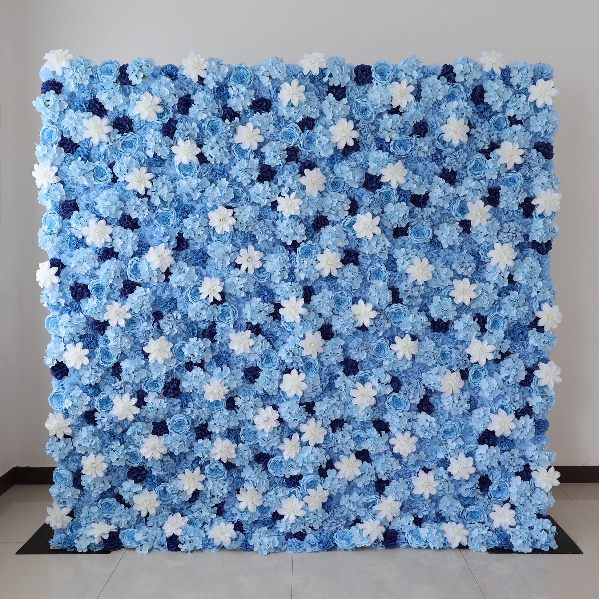 A large artificial flower wall features a stunning arrangement of blue hydrangeas, white blooms, and dark blue blossoms. The dense, uniform pattern creates a serene, elegant backdrop, perfect for events or decorative displays, evoking a calm and sophisticated ambiance. 