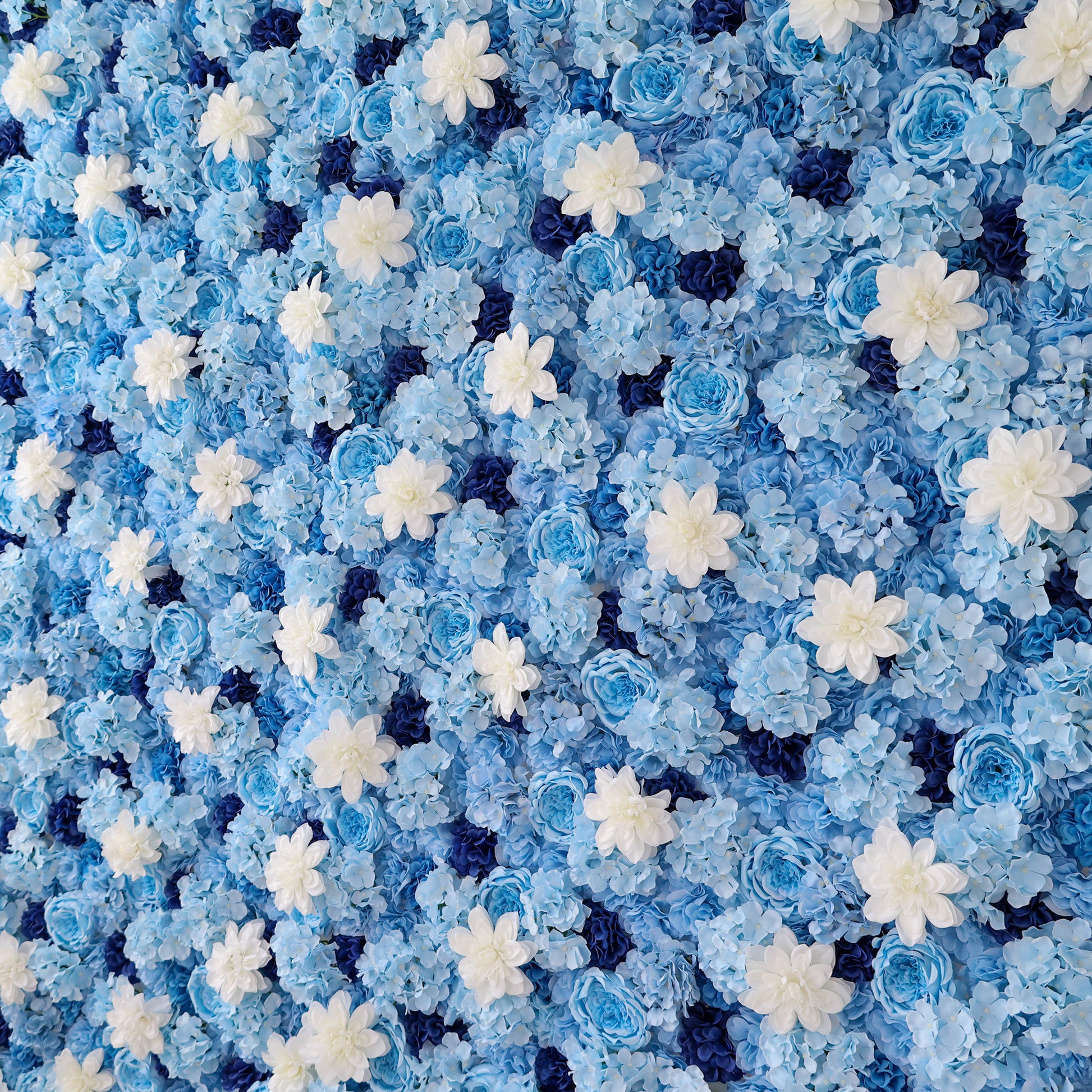 A lush artificial flower wall in soft blue, adorned with white daisy - like blooms and darker blue blossoms. The dense, layered arrangement creates a serene, elegant backdrop, evoking a calm, dreamy ambiance—perfect for events or decorative spaces. 