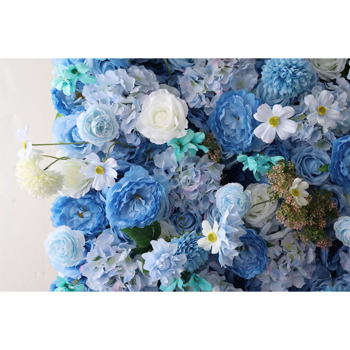 A close - up of an artificial flower wall showcases a beautiful blend of blue blooms. It has soft - toned roses, fluffy chrysanthemums, delicate daisies with yellow centers, and hints of teal foliage. The varied textures and harmonious blue hues create a lush, elegant, and serene floral tapestry, perfect for adding a decorative touch to spaces or events. 