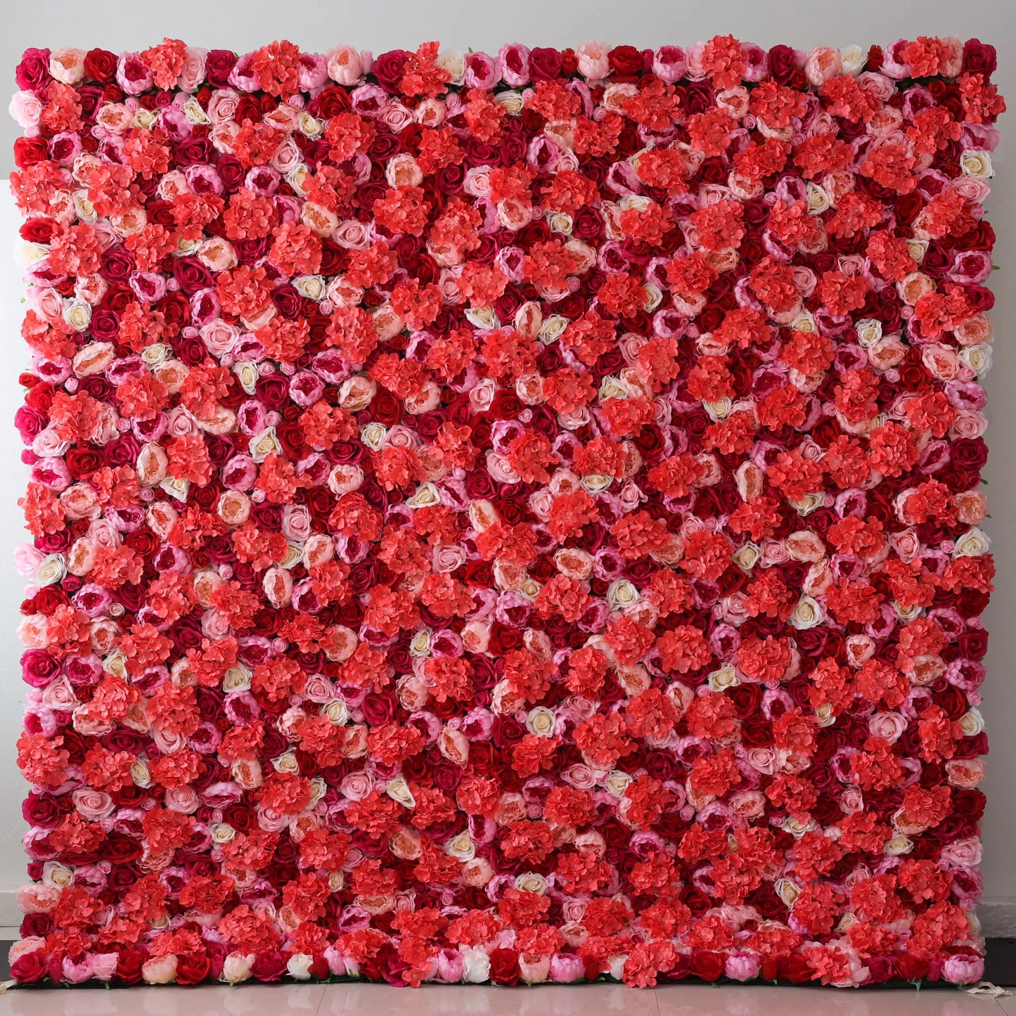 A large artificial flower wall showcases a vibrant mix of roses in shades of coral, pink, white, and deep red. The dense, layered arrangement creates a lush, romantic texture, with blooms tightly packed to form a striking, colorful backdrop. Perfect for adding a lively, decorative touch to events or spaces, exuding warmth and elegance. 