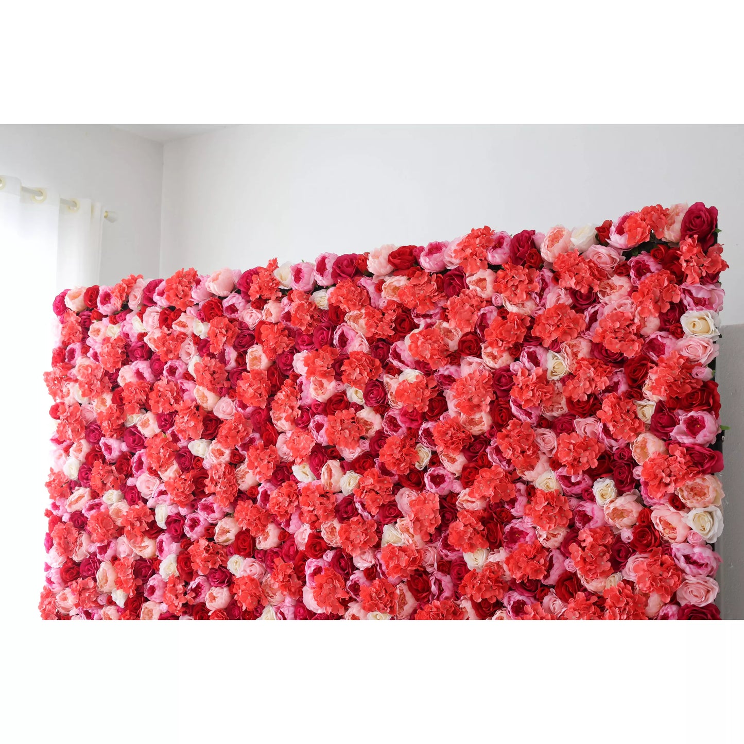 A large artificial flower wall bursts with color! It features a dense mix of roses and blossoms in shades of coral, pink, white, and deep red. The layered arrangement creates a lush, romantic texture, perfect for adding a vibrant, decorative backdrop to events or spaces. 